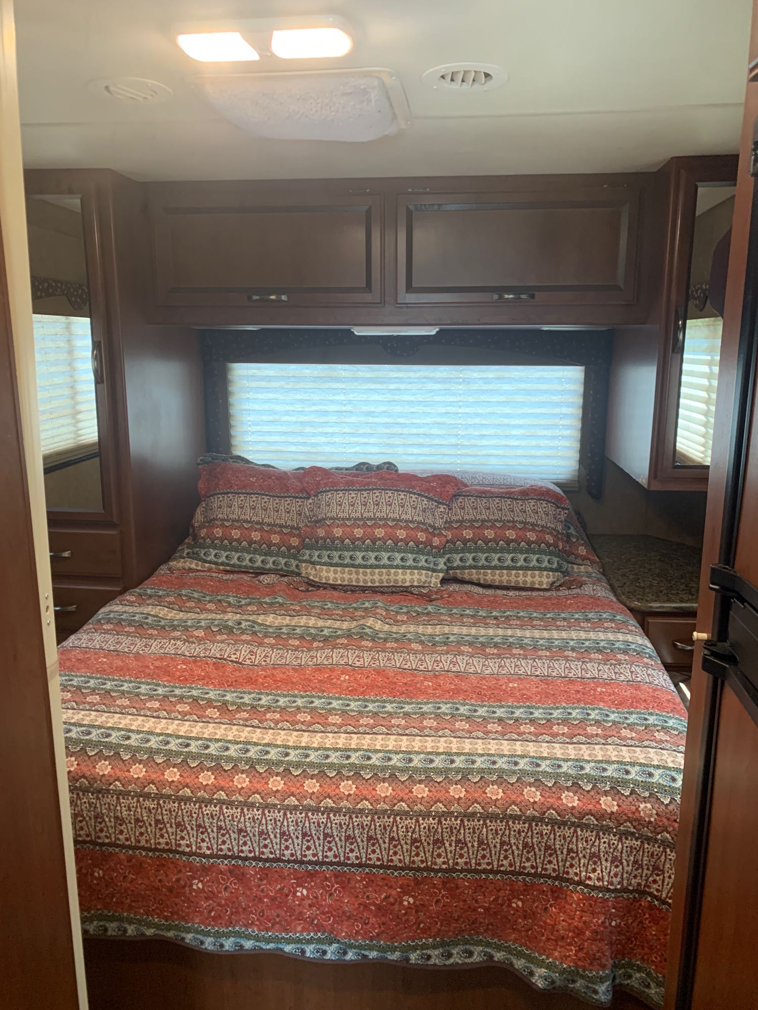 Cozy RV rental bedroom featuring a bed with a colorful quilt, overhead cabinets, and mirrored side units.. Thor Freedom Elite 2015