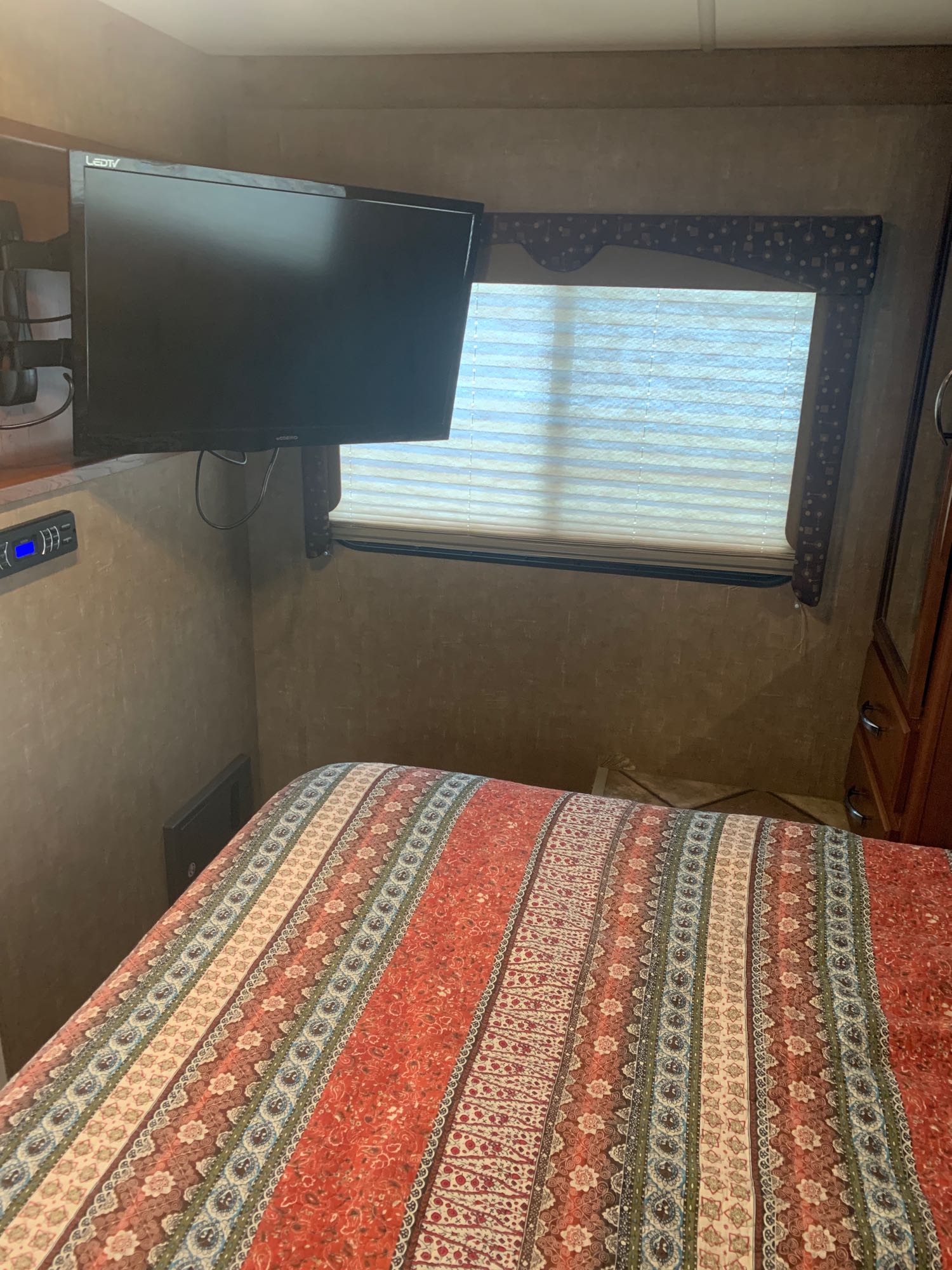 RV rental bedroom interior: a cozy space featuring a vibrant, patterned bed, wall-mounted TV, and window.. Thor Freedom Elite 2015