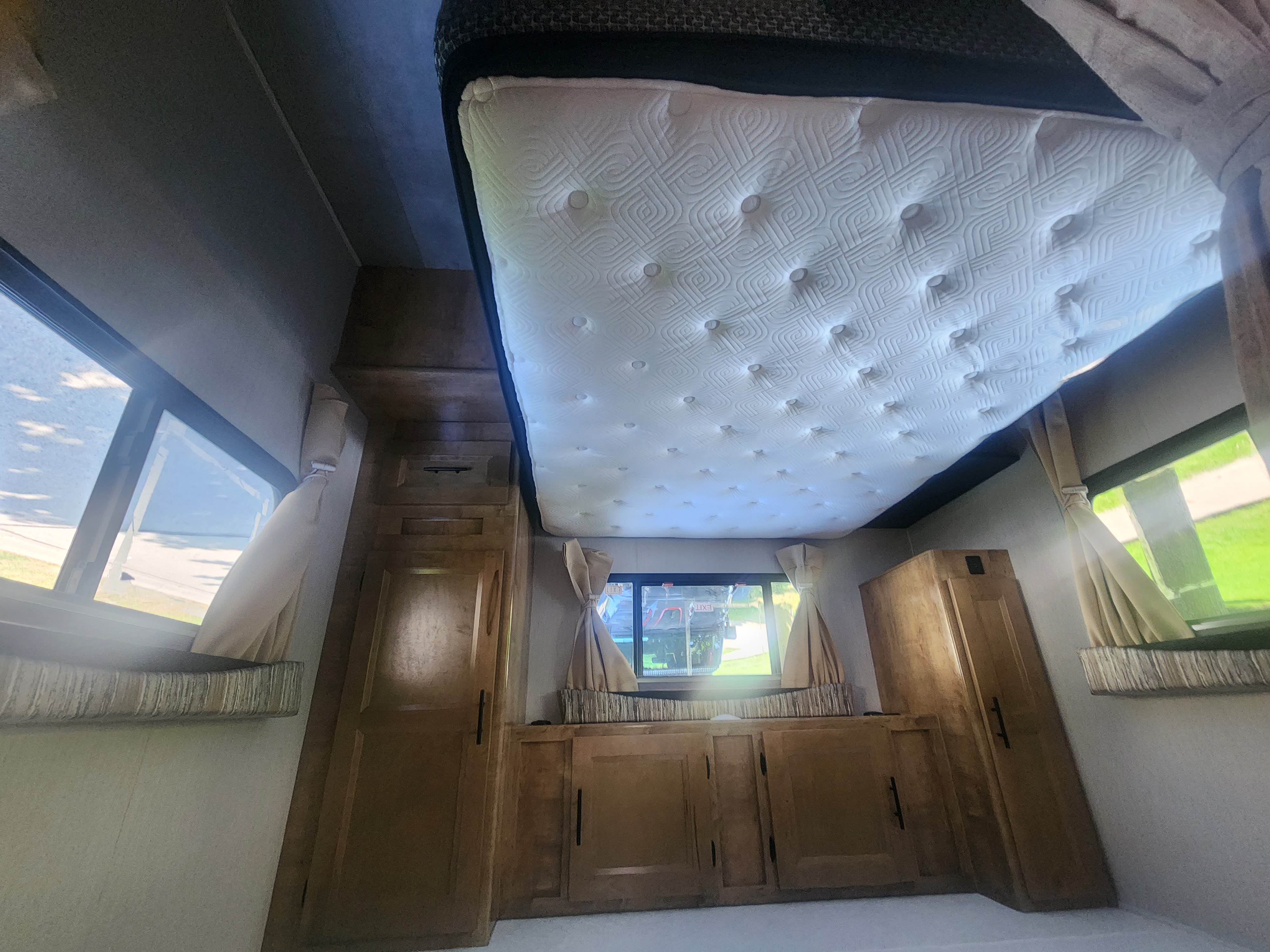 Inside an RV rental: a cozy bedroom featuring a unique drop-down bed, windows with curtains, and ample wooden storage cabinets.. Lepercaune 27qb 2022