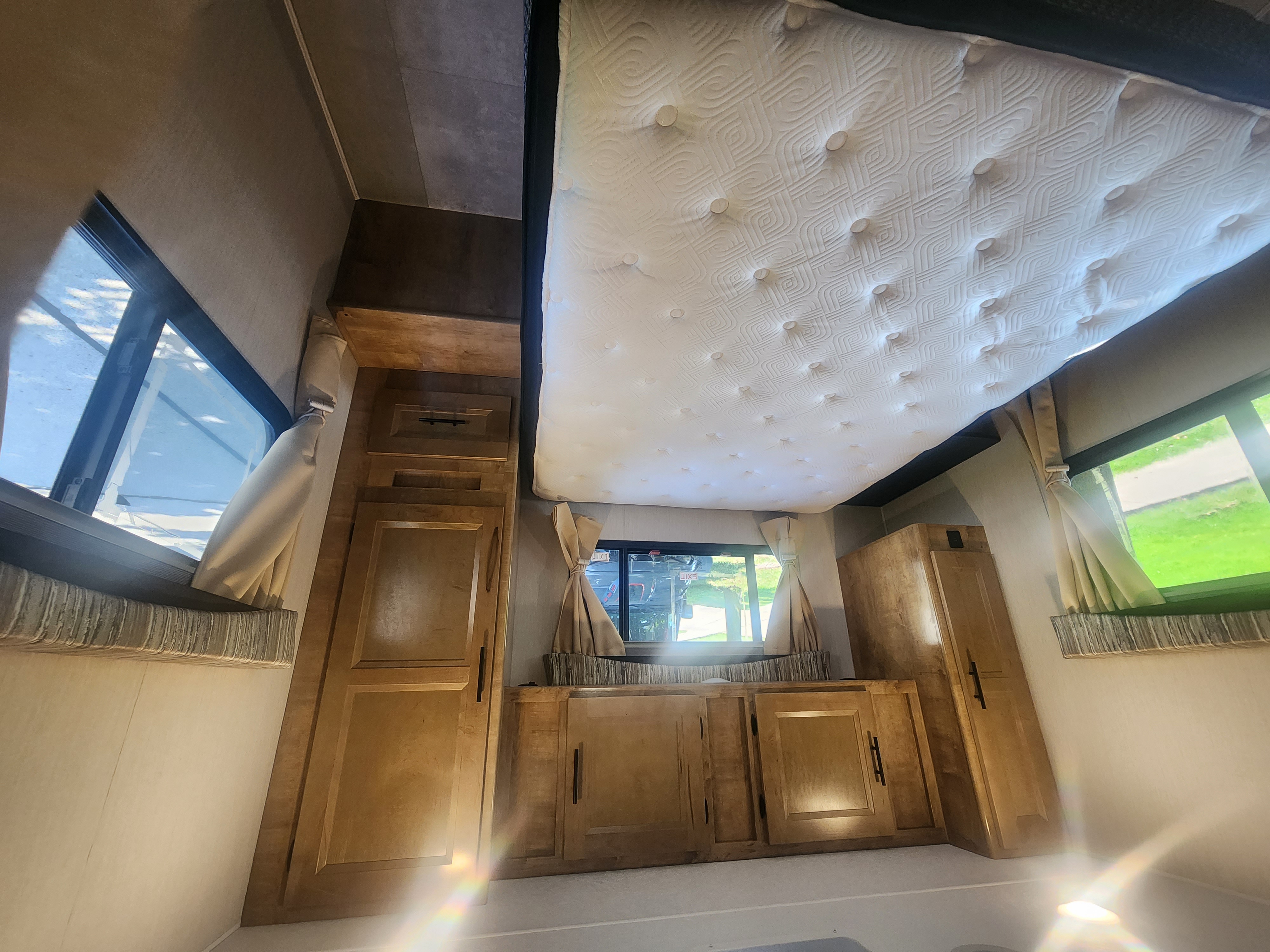 Spacious RV rental bedroom featuring a comfortable loft bed, ample wooden cabinets, and bright windows. Ideal for travel.. Lepercaune 27qb 2022