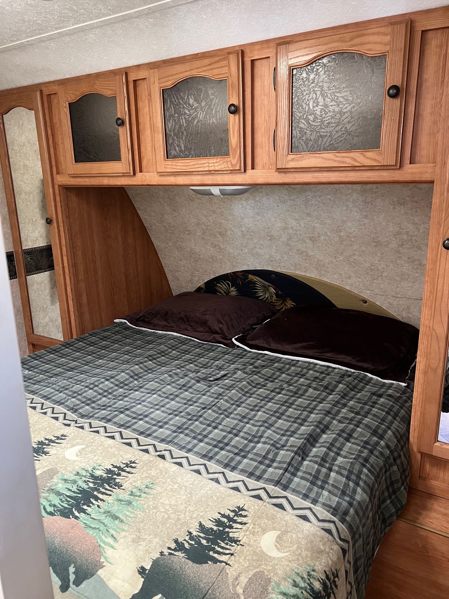 Explore this comfy RV rental bedroom. Features plaid bedding, wooden cabinets, and ample storage for travel.. Keystone RV Passport 2007