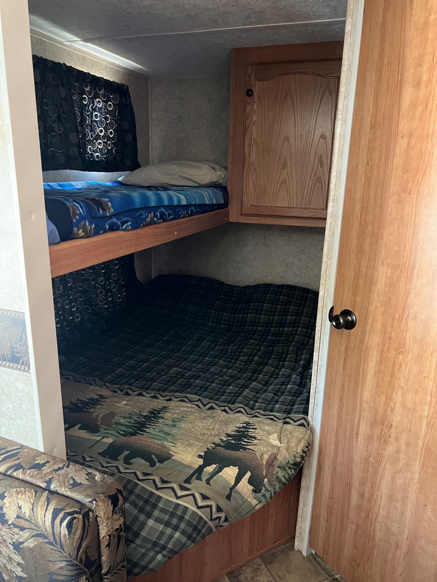 Cozy bunk beds in an RV rental, featuring an upper and lower bunk with blankets, cabinet storage, and an adjacent couch.. Keystone RV Passport 2007