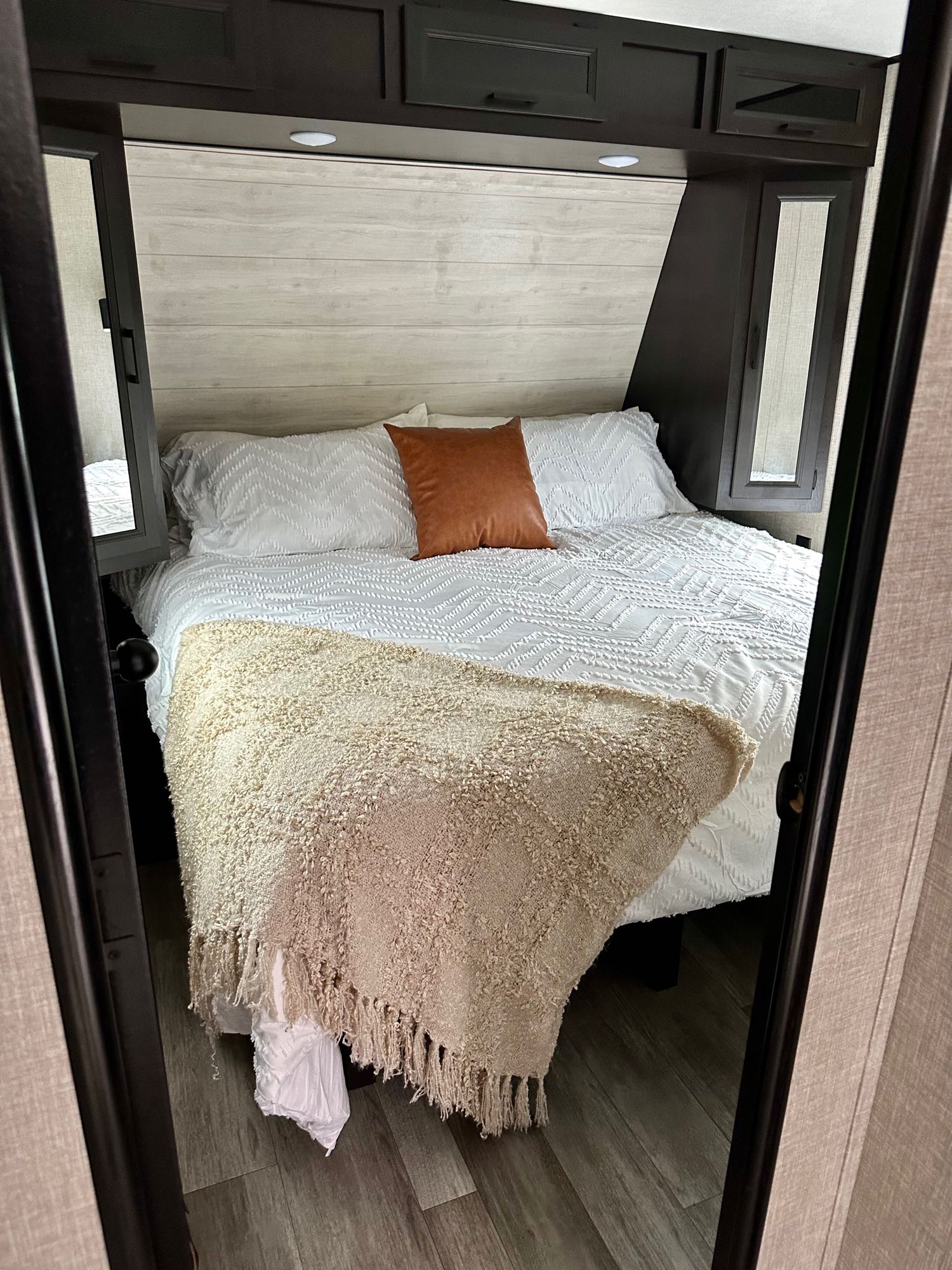 Cozy RV rental bed setup with white bedding, a rust accent pillow, cream throw, overhead cabinets, and wood-look floor.. Jayco Jay Flight 2022