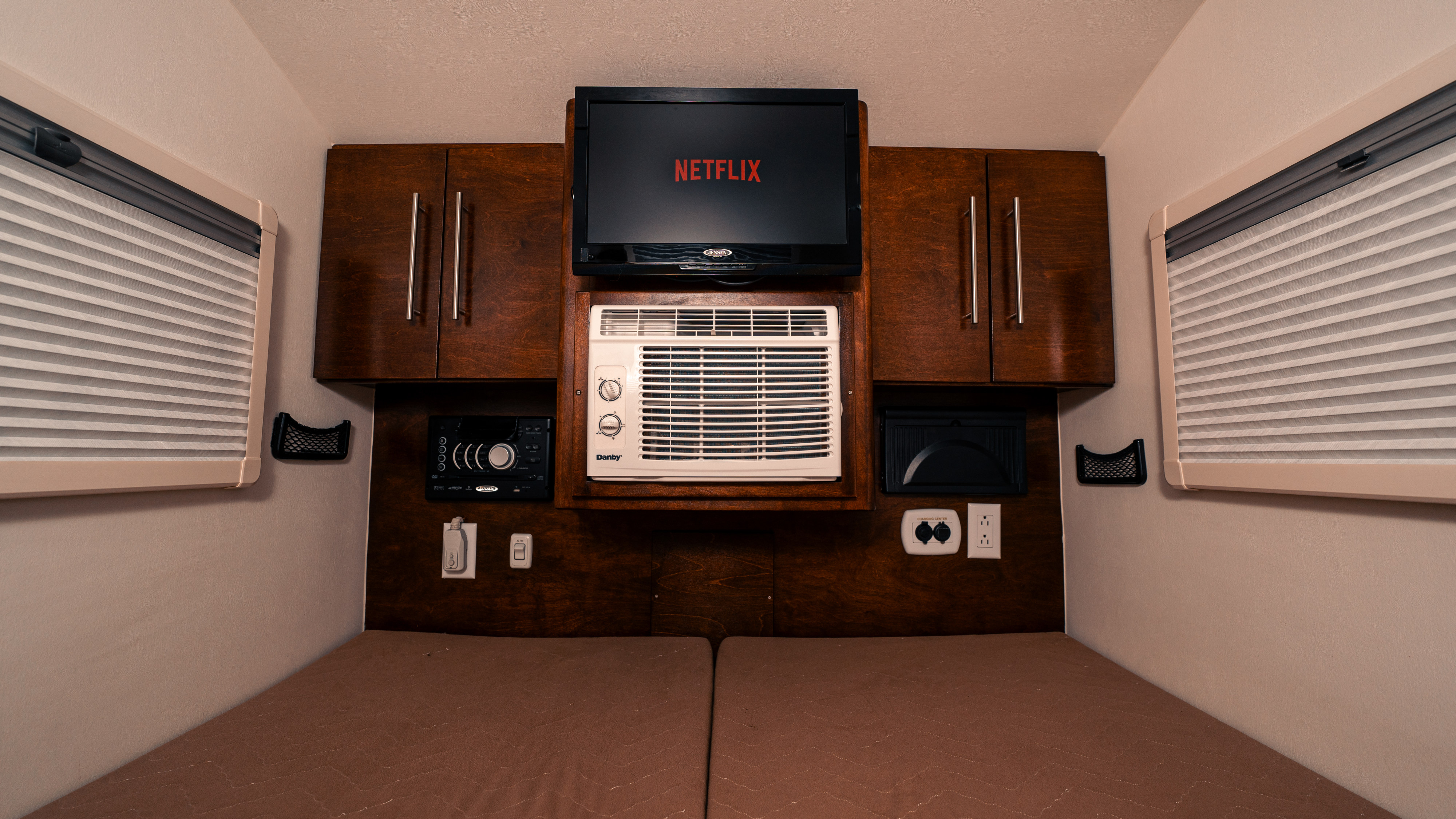 RV rental interior featuring a TV displaying Netflix, an AC unit, twin beds, and overhead cabinets.. nuCamp T@G 2017