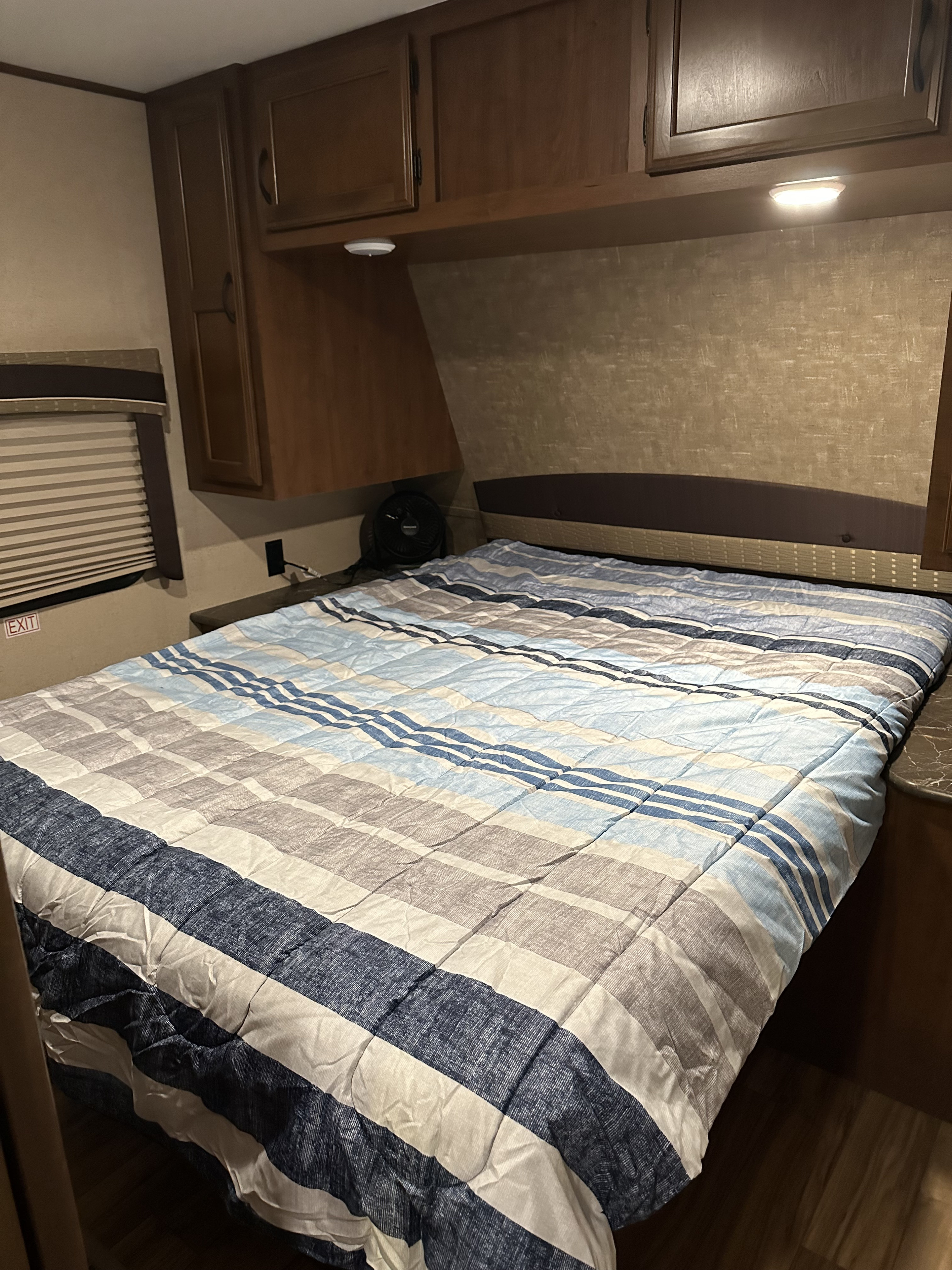 Compact RV rental bedroom with a striped comforter, overhead cabinets, and an emergency exit sign.. Jayco Jay Flight 2016