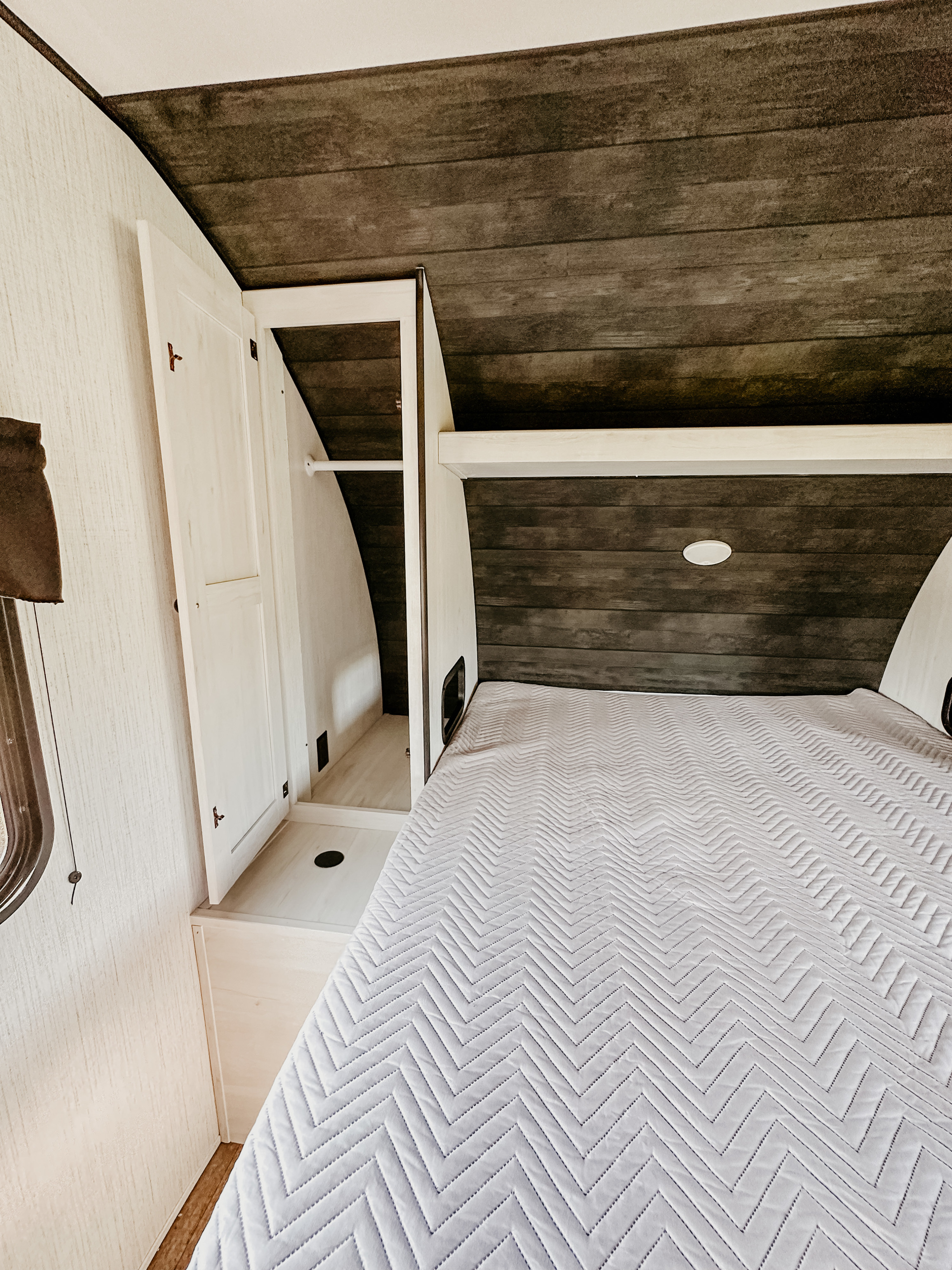 Clean RV rental bedroom with a white chevron-patterned bed, dark wood paneling, and an open closet with hanging space.. Heartland RVs Trail Runner 2022