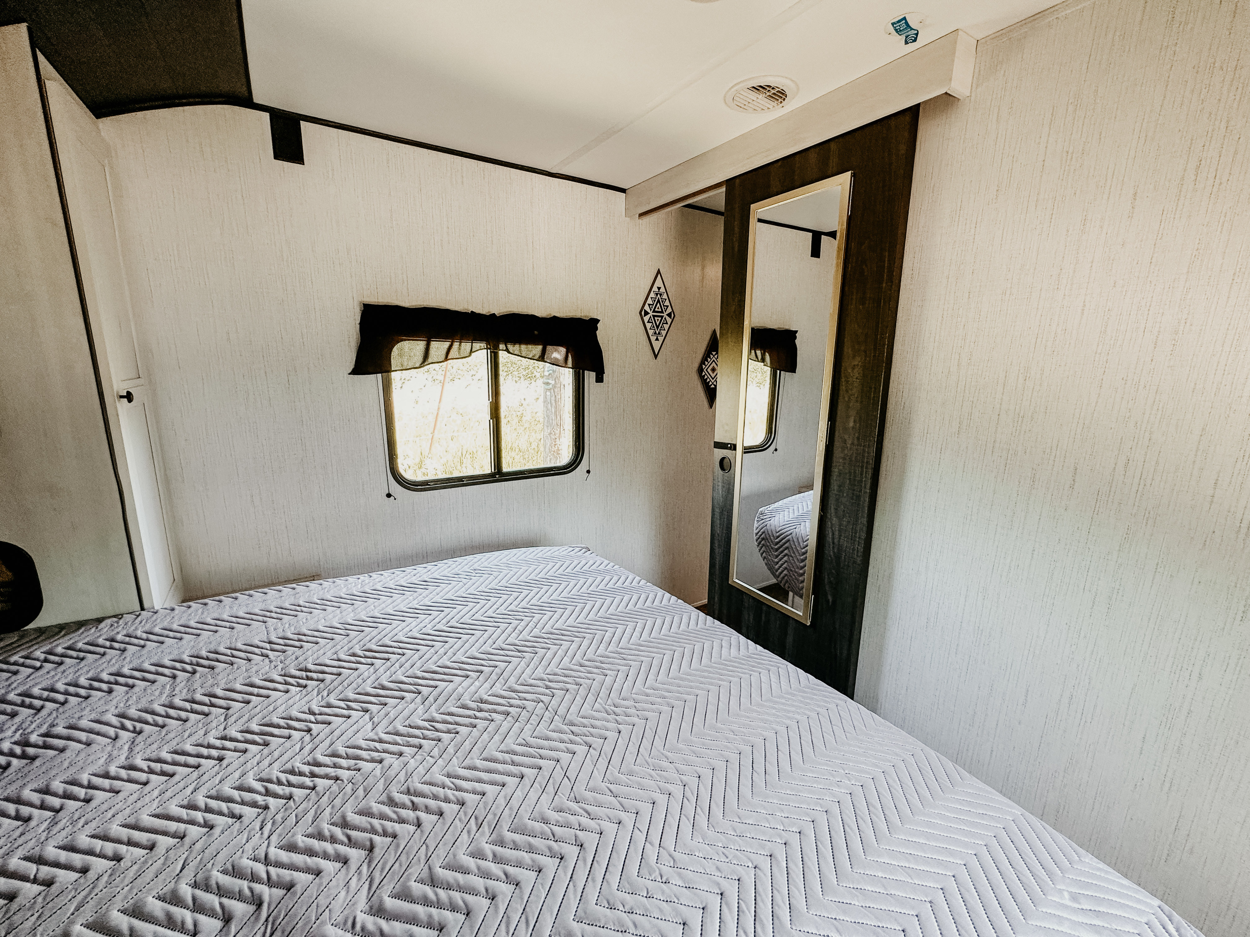 Cozy RV rental bedroom with a chevron-patterned bed, window, and full-length mirror for comfortable travel.. Heartland RVs Trail Runner 2022
