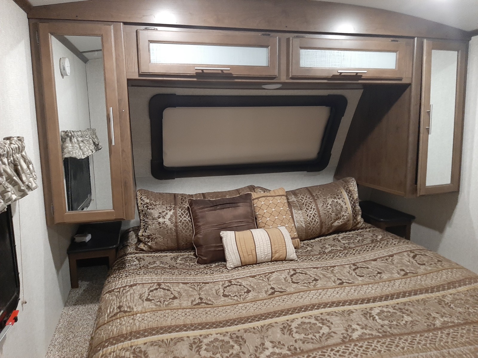Step inside this cozy RV rental bedroom. Features a comfortable bed with ornate bedding, overhead cabinets, and side mirrors.. Keystone Cougar 2019