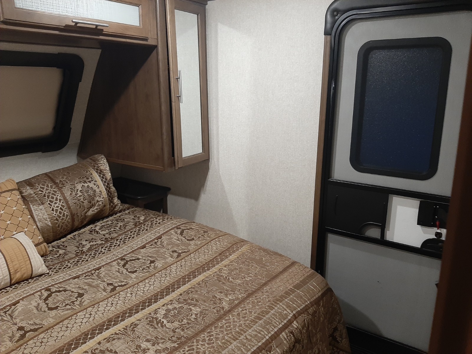 Cozy RV rental bedroom with a patterned bed, overhead cabinets, and a compact interior door.. Keystone Cougar 2019