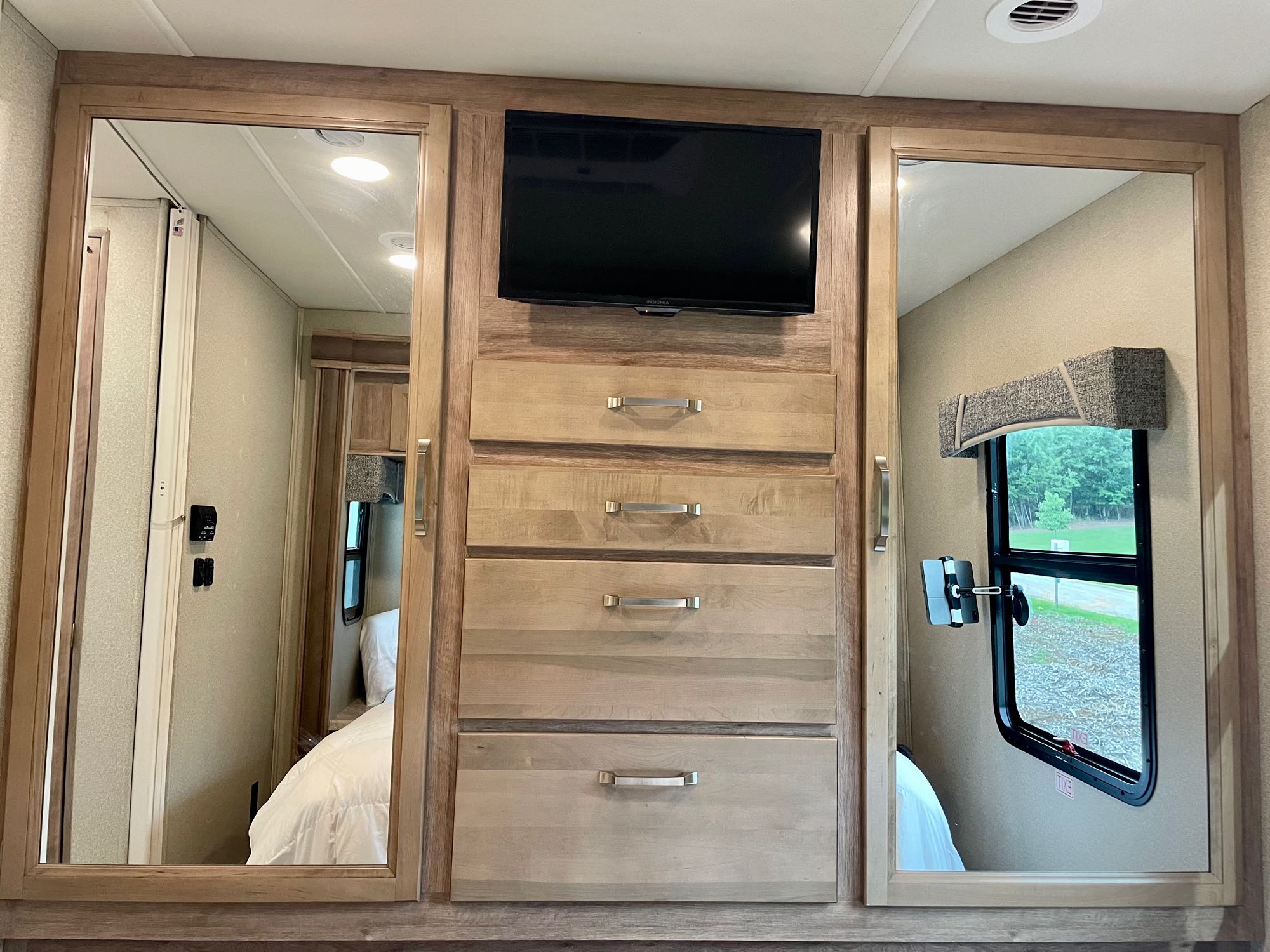 RV rental bedroom: light wood cabinetry with TV, dresser drawers, and mirrored wardrobes reflecting the interior and exterior.. Jayco Greyhawk Prestige 2020