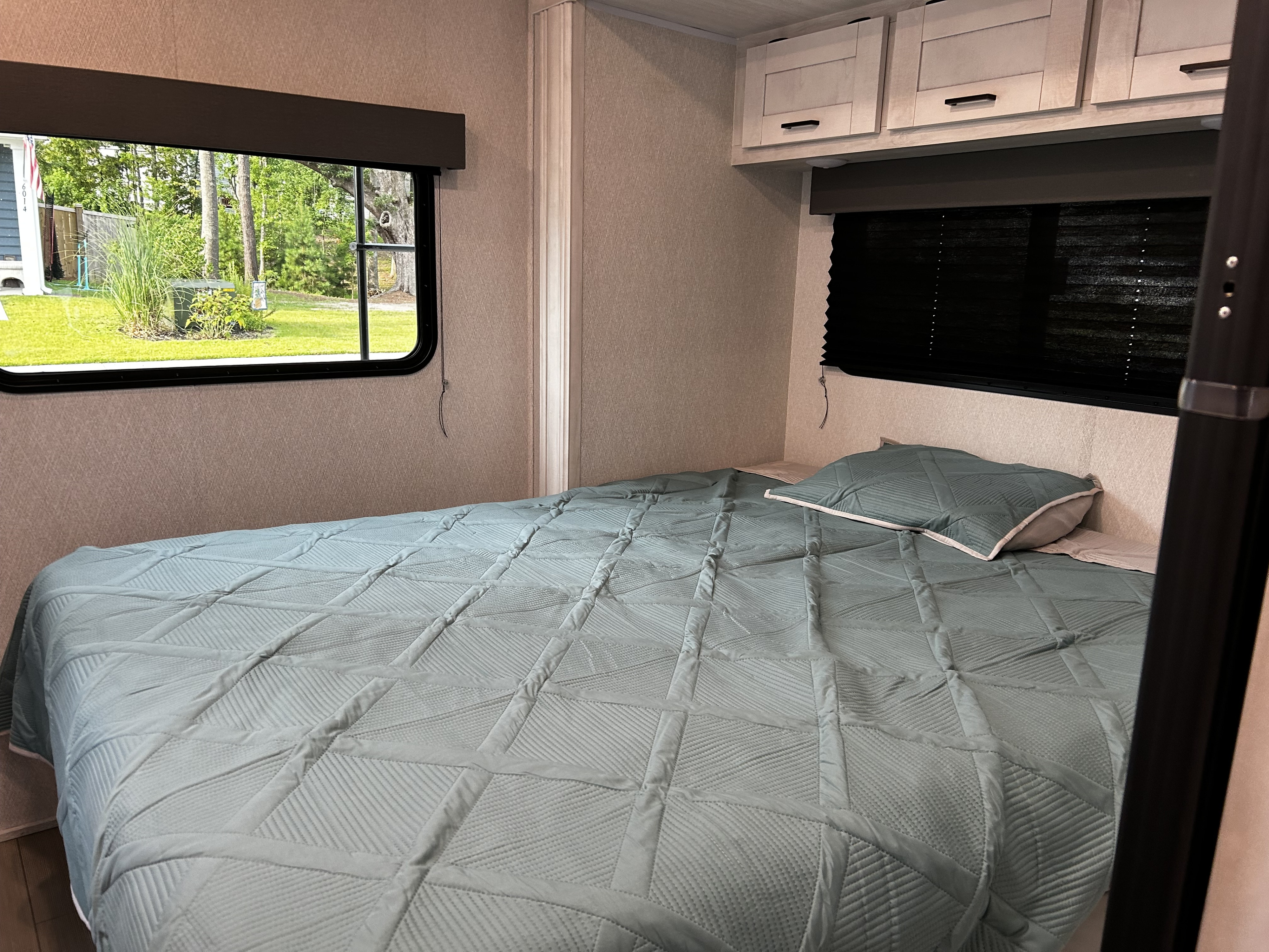 Cozy RV rental bedroom featuring a comfortable bed, window with outdoor views, and convenient overhead storage cabinets.. Coachman Entrada East to West 2200S 2023