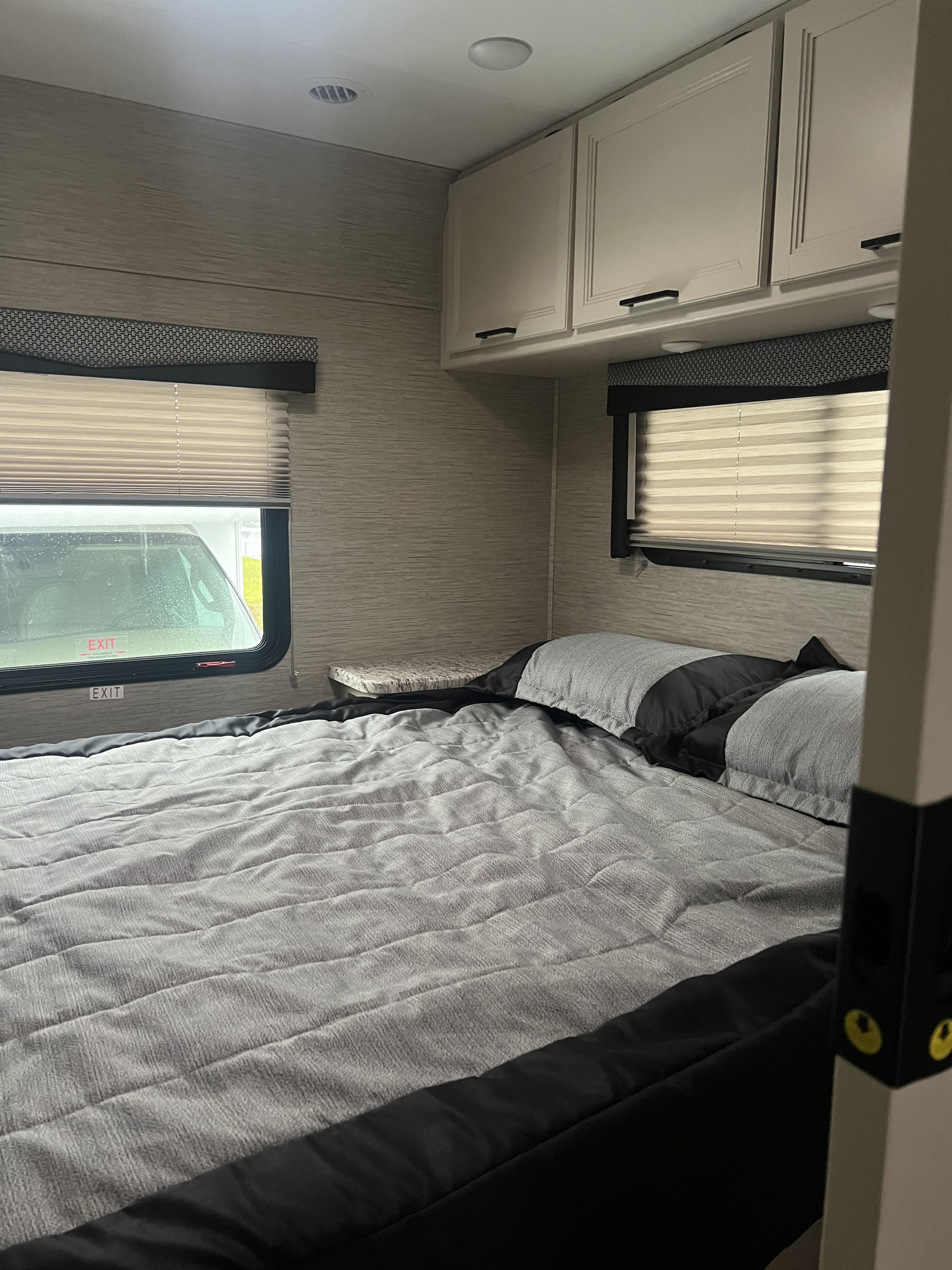 Step inside this RV rental's comfortable bedroom, featuring a spacious bed, overhead storage, and natural light from large windows.. Thor Freedom Elite 2023