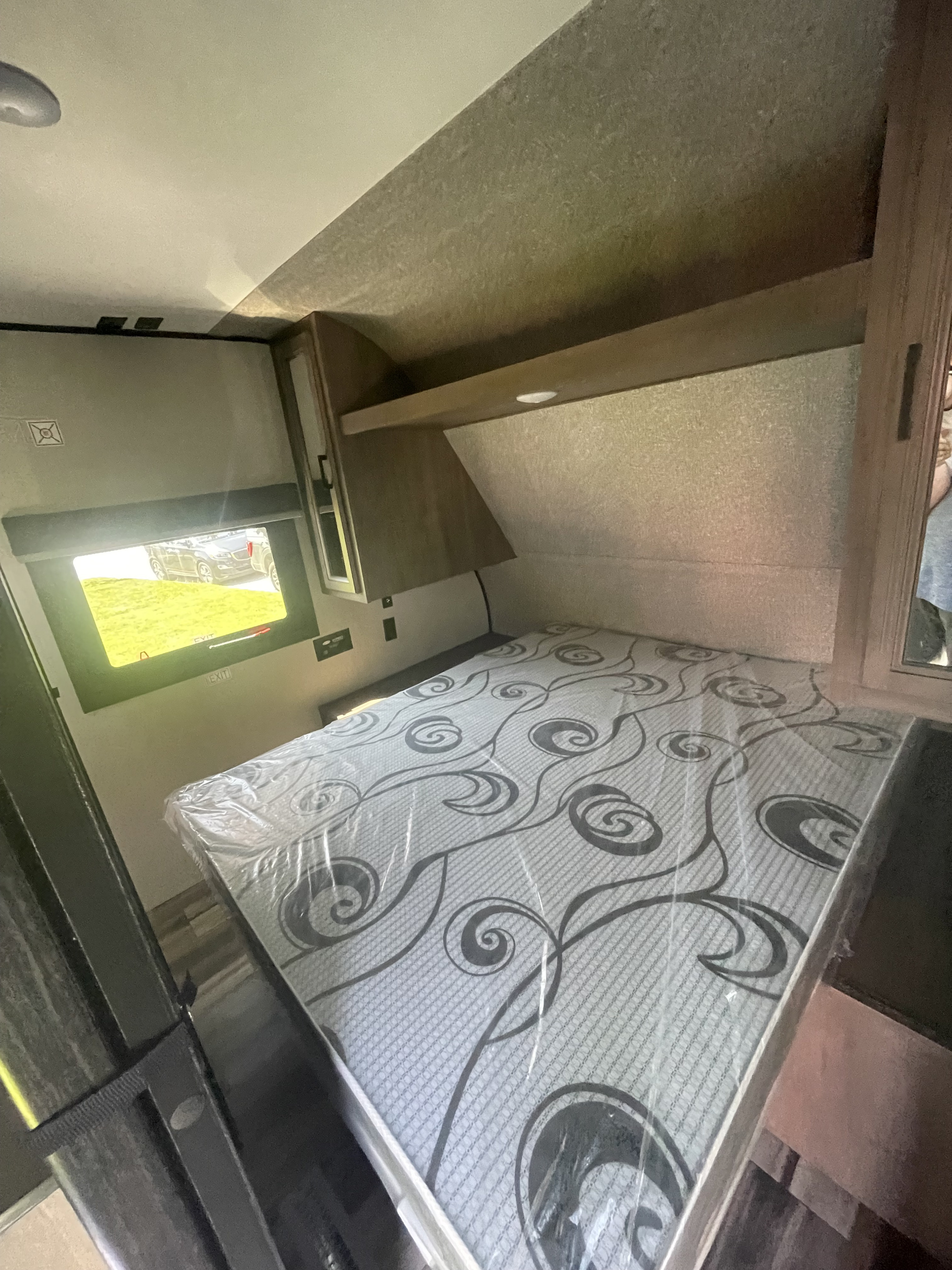 Explore this RV rental's cozy bedroom, showcasing a fresh, plastic-wrapped mattress, overhead storage, and a window.. Highland Ridge RV Open Range 2022