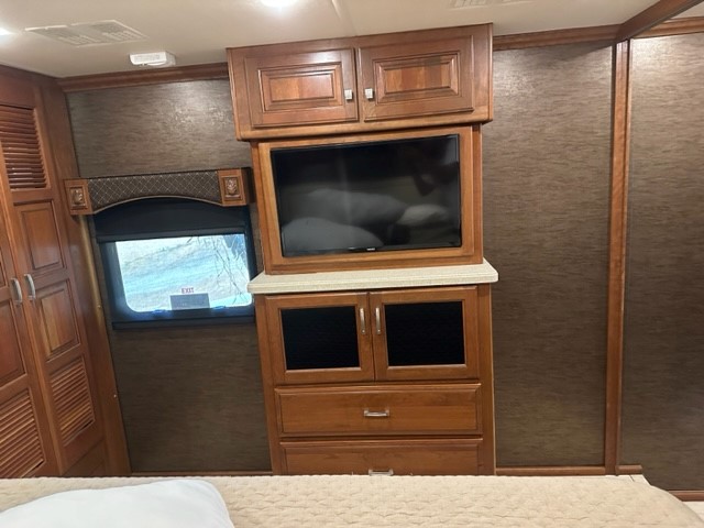 RV rental bedroom interior showcasing an entertainment center with TV, cabinets, and a window. Road comfort.. Holiday Rambler Endeavor 2017