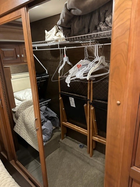RV rental interior: A compact closet features a hanging rod, hangers, and top shelf. Folded chairs are below. Mirrored door shows bedroom.. Holiday Rambler Endeavor 2017