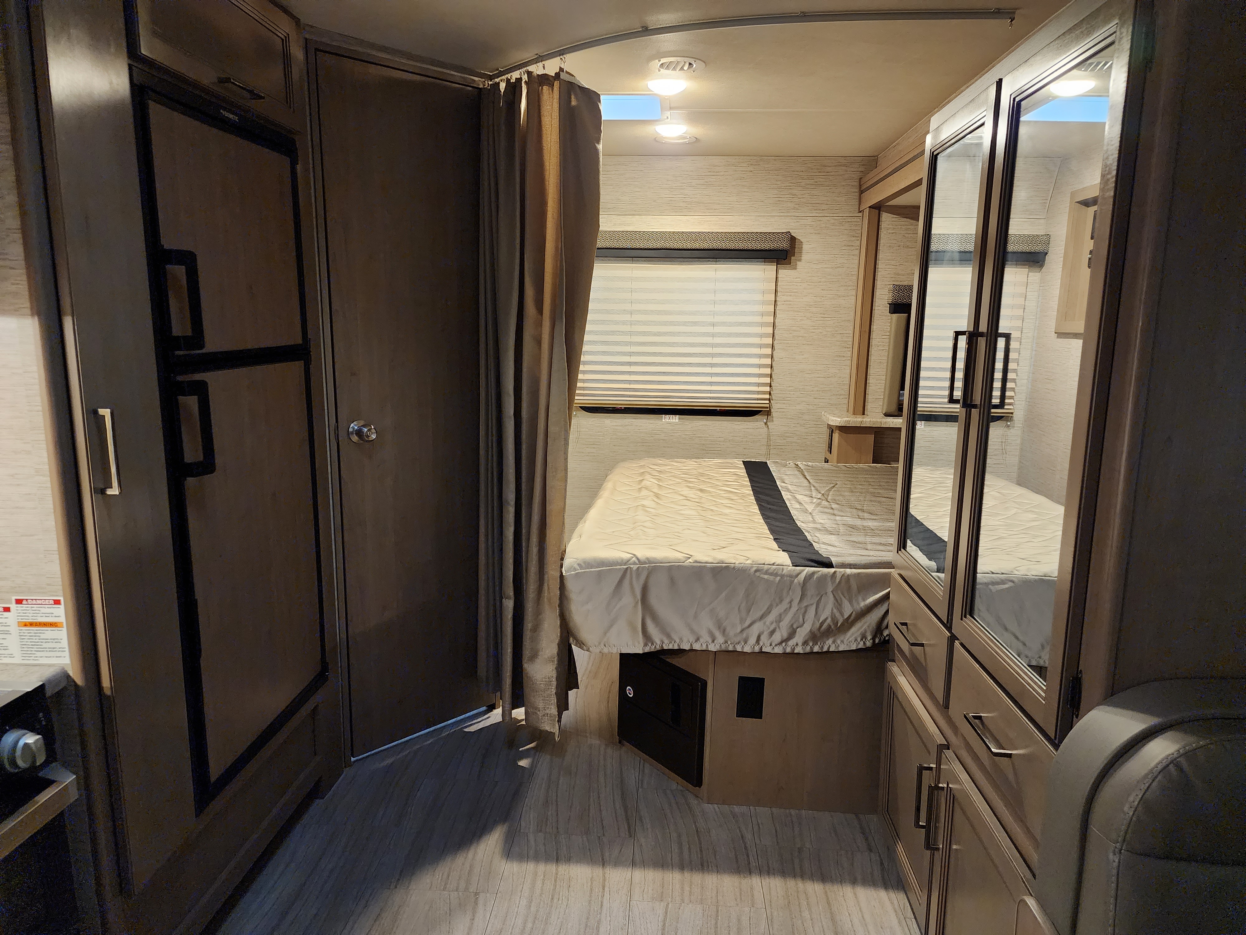 Step inside this cozy RV rental bedroom. Features include a bed, fridge, mirrored closet, and window with blinds.. Thor Daybreak 2021