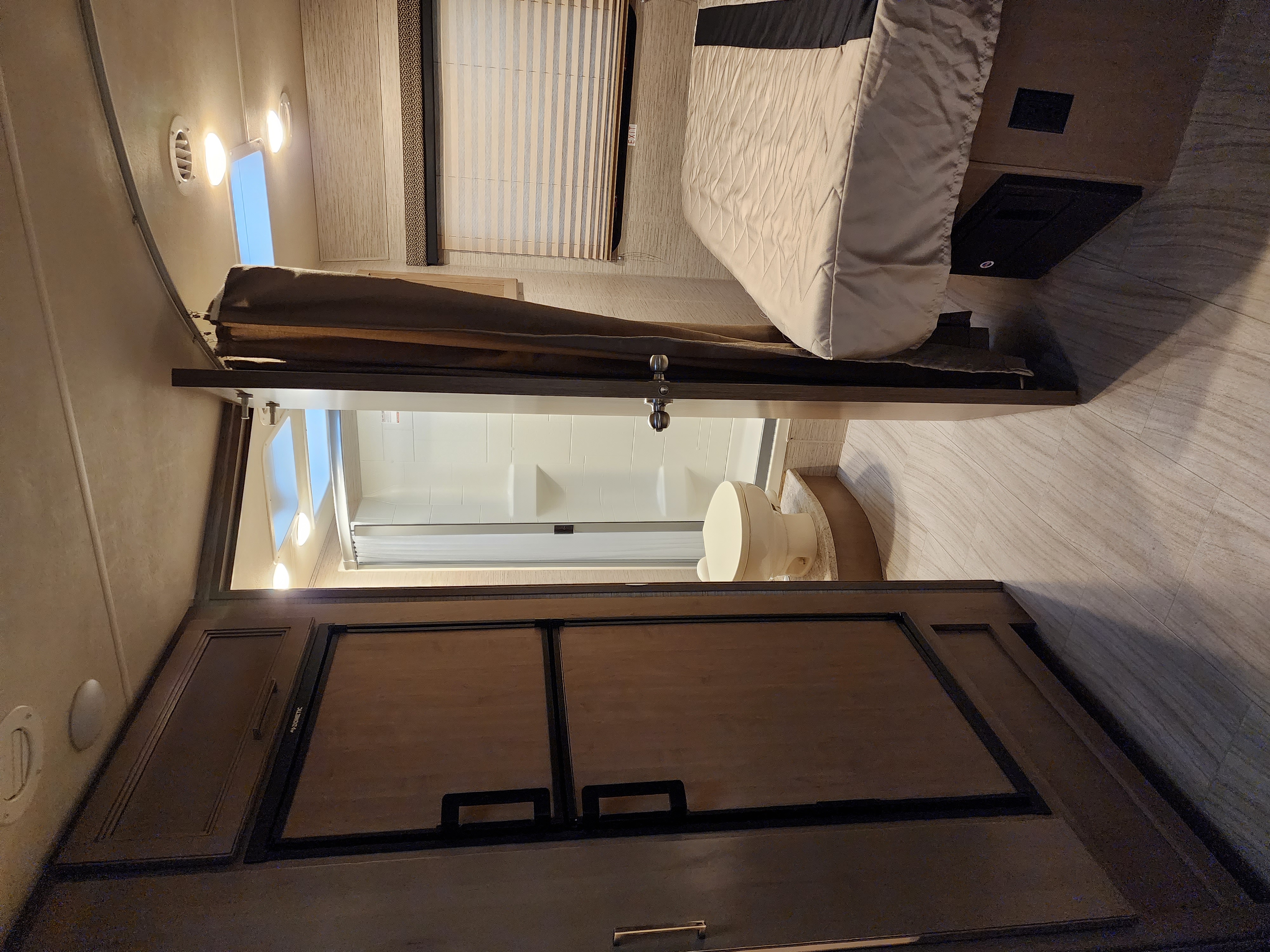RV rental interior featuring a cozy bed, compact bathroom with toilet and shower, and built-in refrigerator.. Thor Daybreak 2021