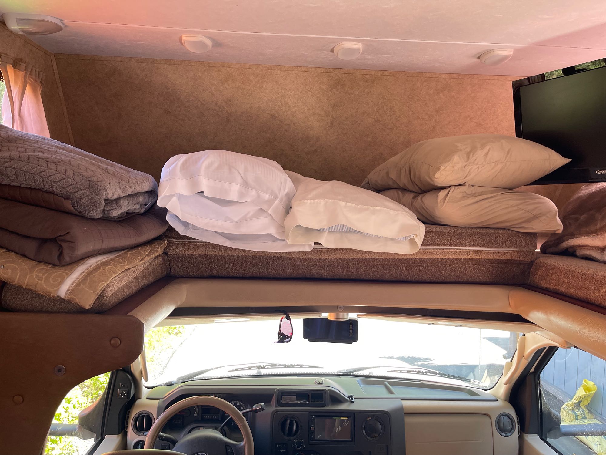 An RV rental's cozy interior, showing the overhead bunk with bedding, a TV, and the driver's cabin area.. Forest River Sunseeker 2013