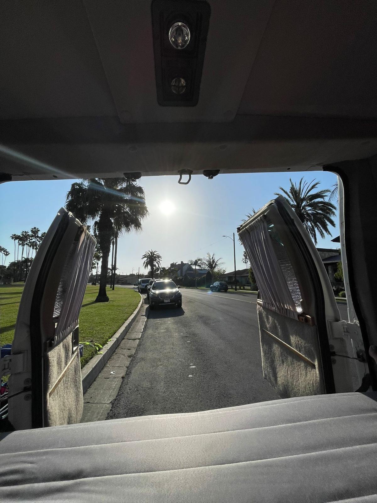 Inside an RV rental, looking out the open rear doors at a sunny, palm-lined street with parked cars. Ready for travel!. Ford SV 1994