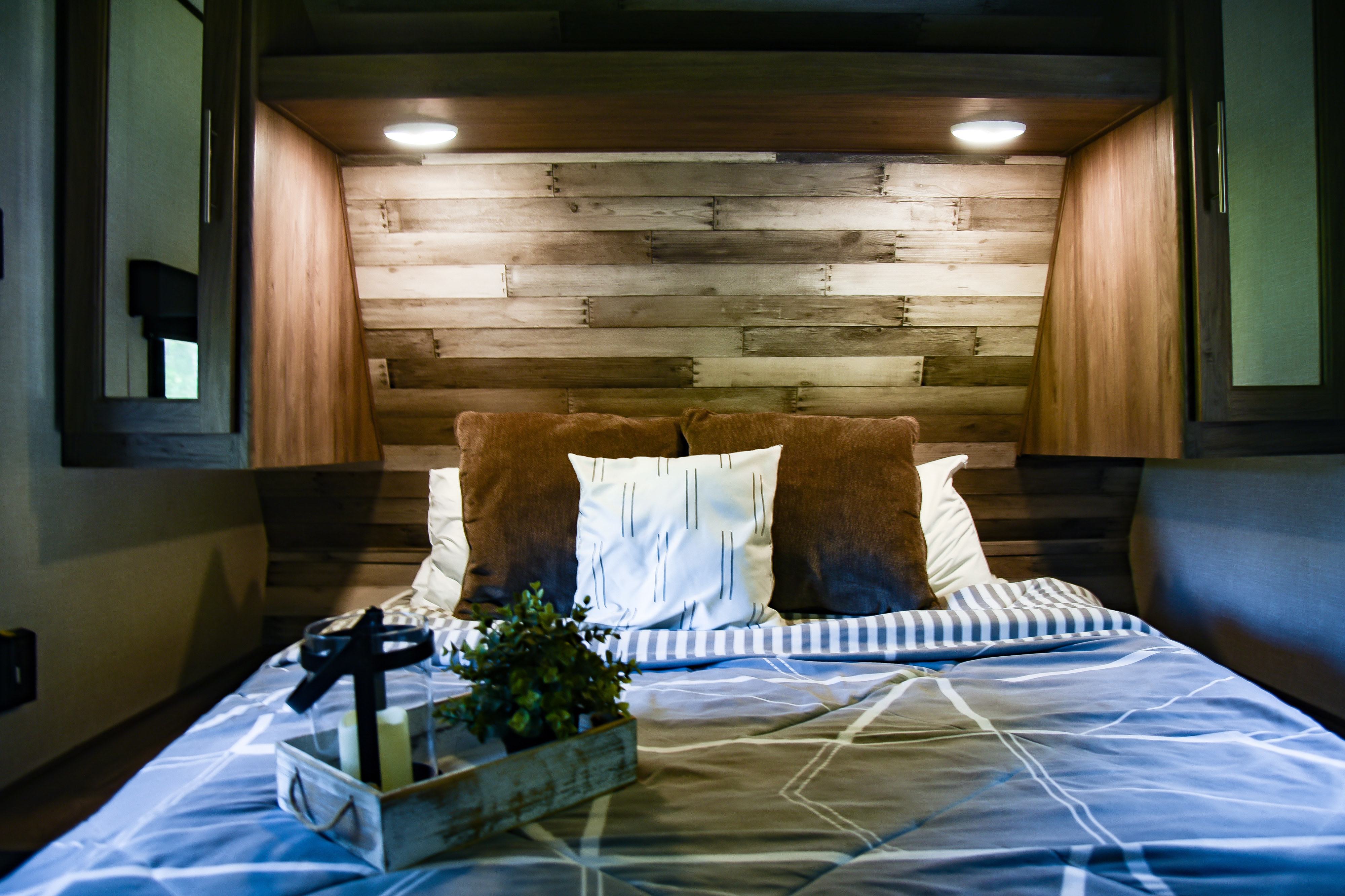 Relax in this modern RV rental bedroom featuring a chic reclaimed wood headboard, ambient lighting, and cozy bedding.. Crossroads RV Zinger 2023