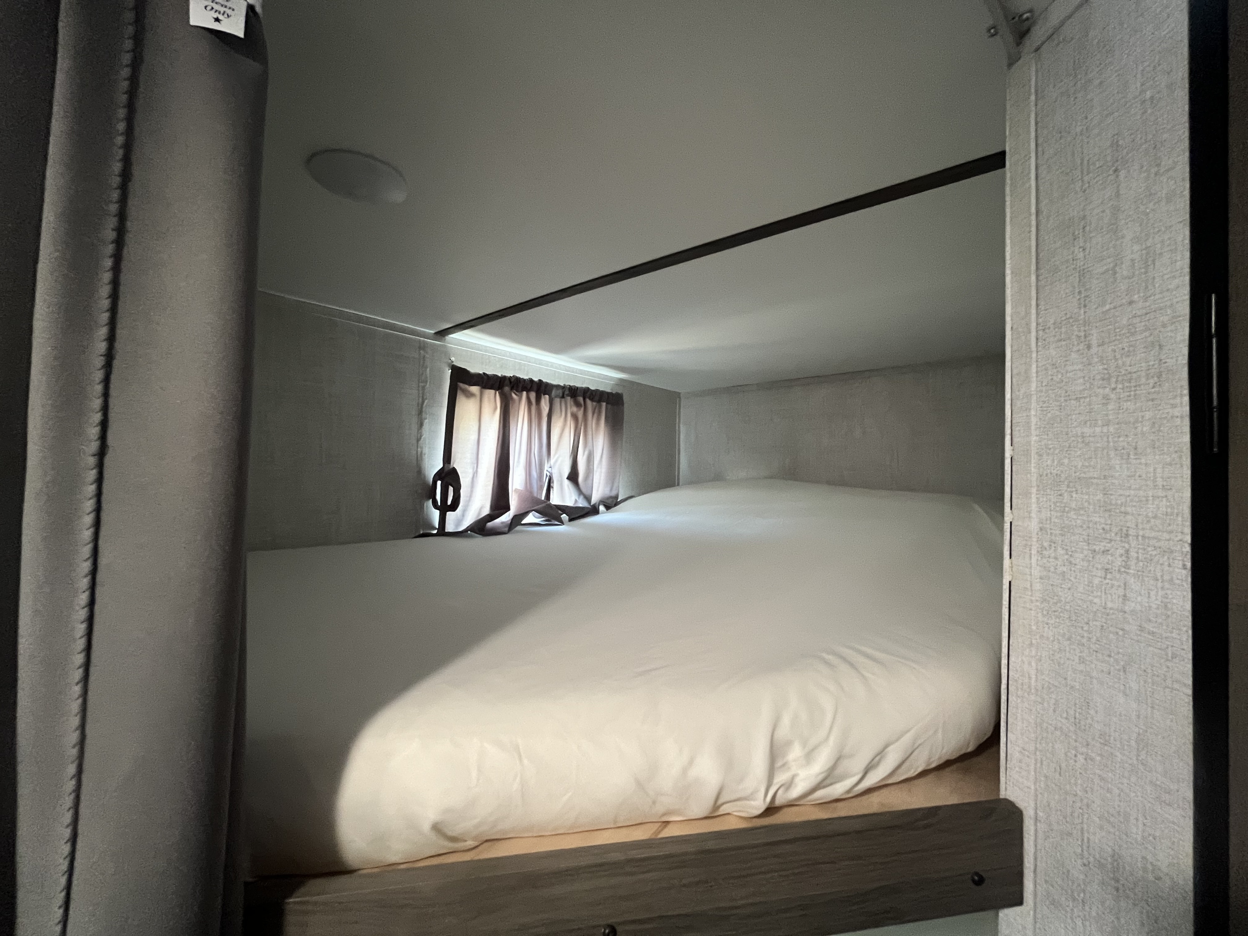 Experience a comfortable night in this compact RV rental bunk bed, featuring white linens and privacy curtains.. Gulf Stream Kingsport 2022