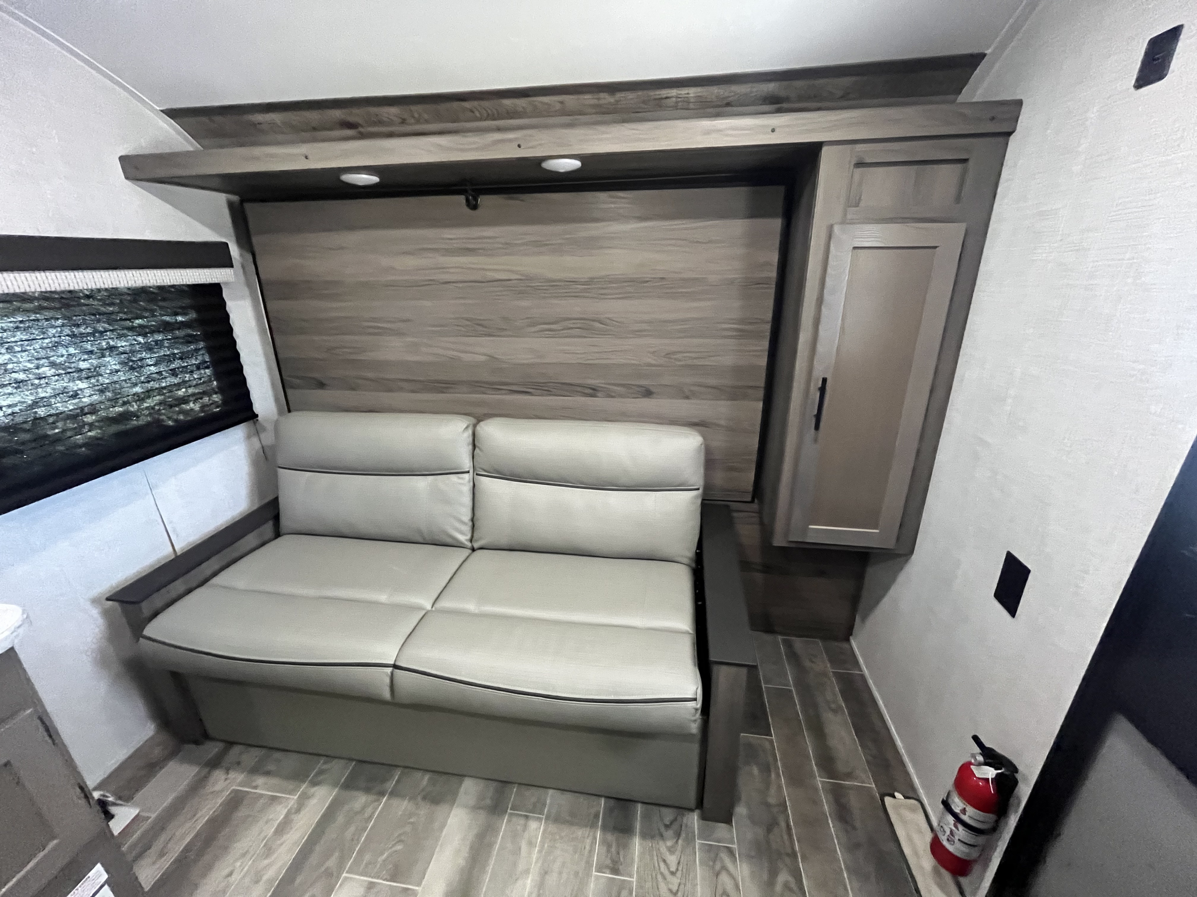 RV rental interior featuring a versatile grey sofa, overhead lights, a side cabinet, and a visible fire extinguisher.. Gulf Stream Kingsport 2022