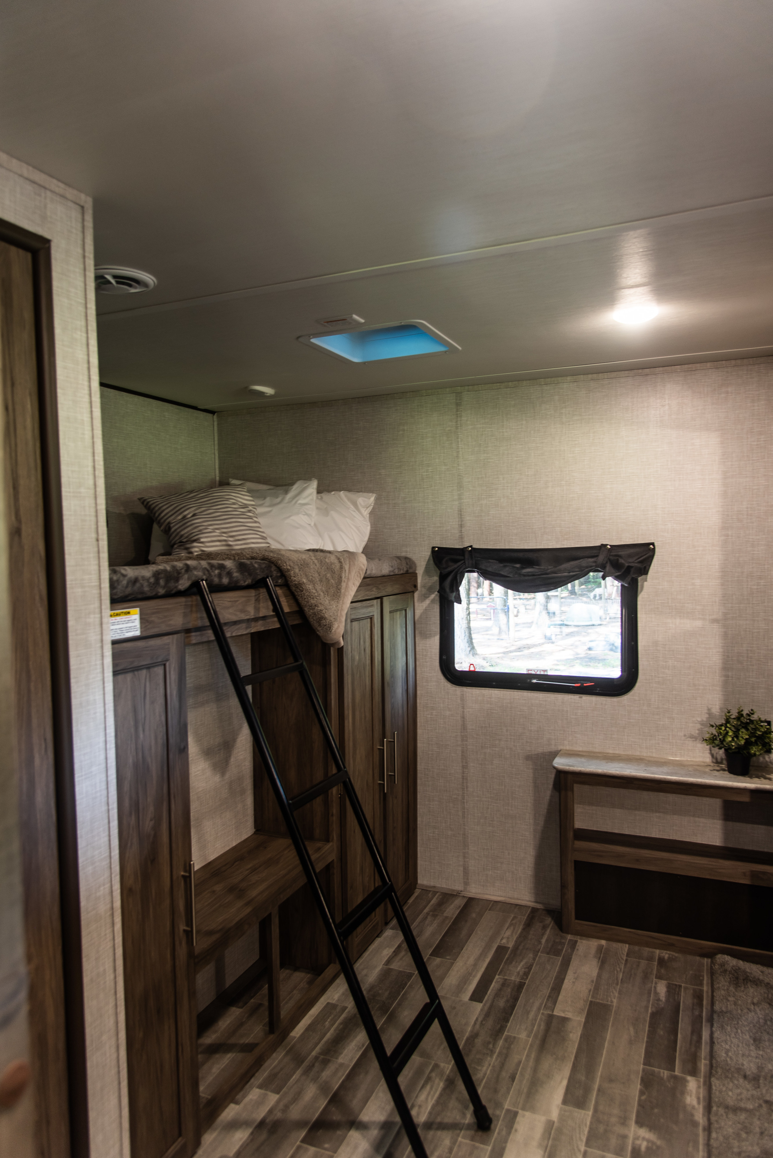 RV rental interior features bunk beds with a ladder, wood-look floor, window view, and built-in storage.. Crossroads RV Zinger 2023