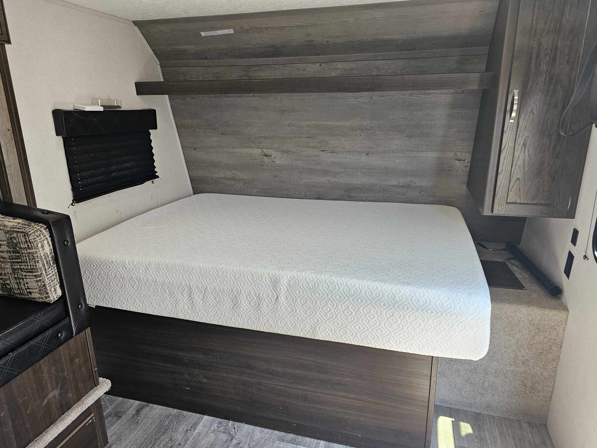 Clean RV rental bedroom featuring a fresh white mattress, dark wood accents, and window. Perfect for your next adventure.. Keystone RV Springdale 2020