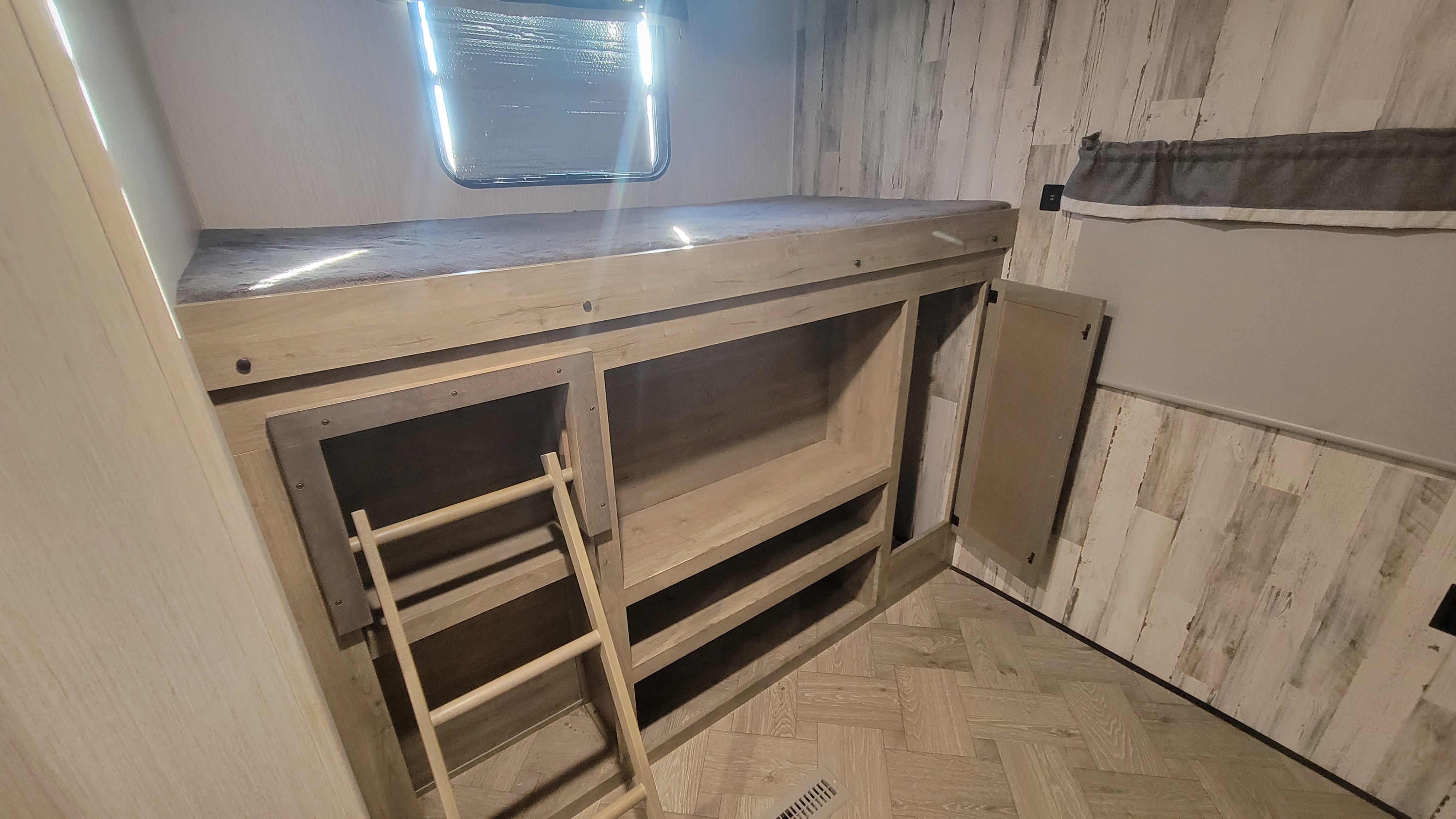 Bright RV rental interior showing bunk beds with a window, ladder, and built-in storage shelves in a modern, wood-toned space.. Forest River Palomino Puma 2021