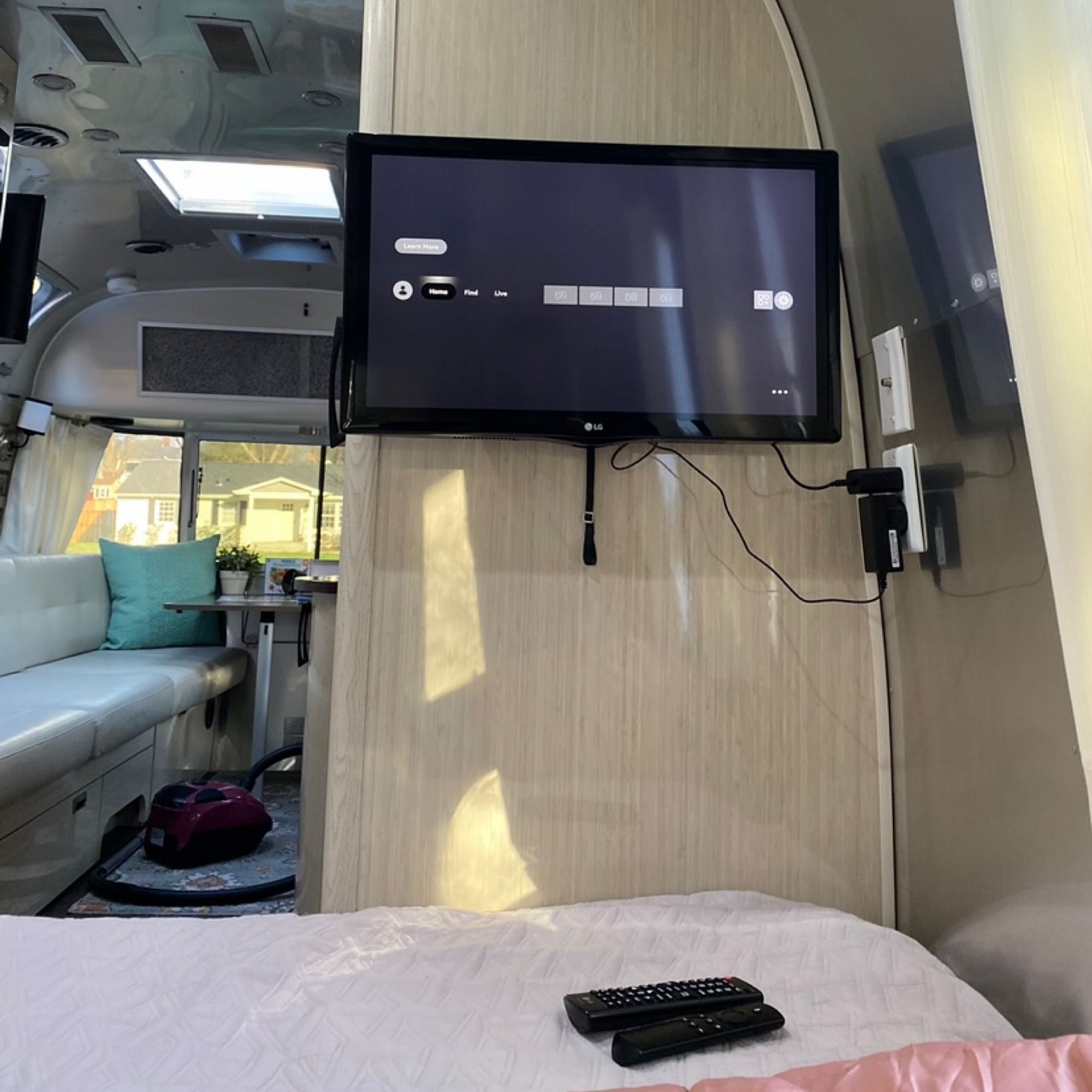 Inside a modern RV rental: a bright living space with a dinette, mounted TV, and a comfortable bed in the foreground.. Airstream International 2016