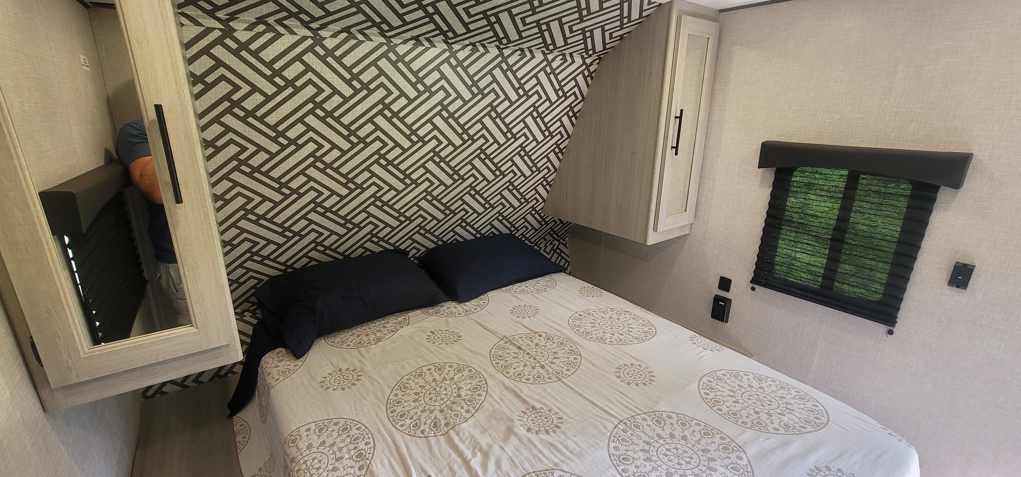 Cozy RV rental bedroom interior featuring a comfortable bed, patterned wall, storage cabinets, and a window.. Crossroads RV Zinger Lite 2023