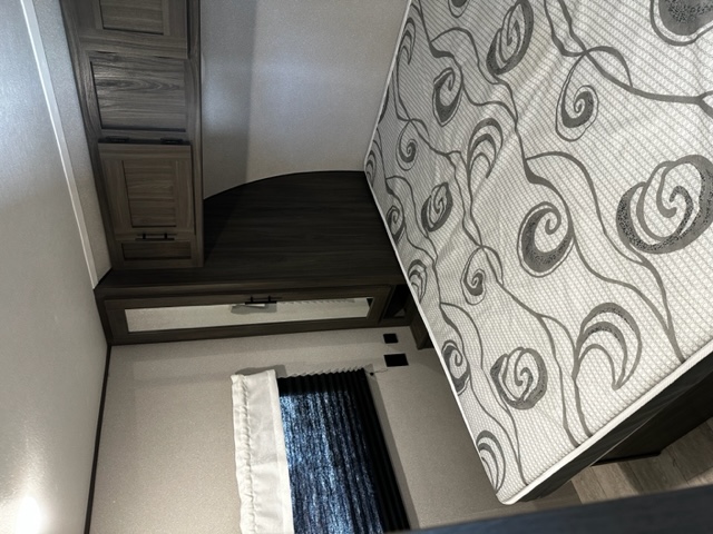 Compact RV rental bedroom features a patterned mattress, wood cabinets, and a mirror, providing cozy travel comfort.. Forest River Shasta 2021
