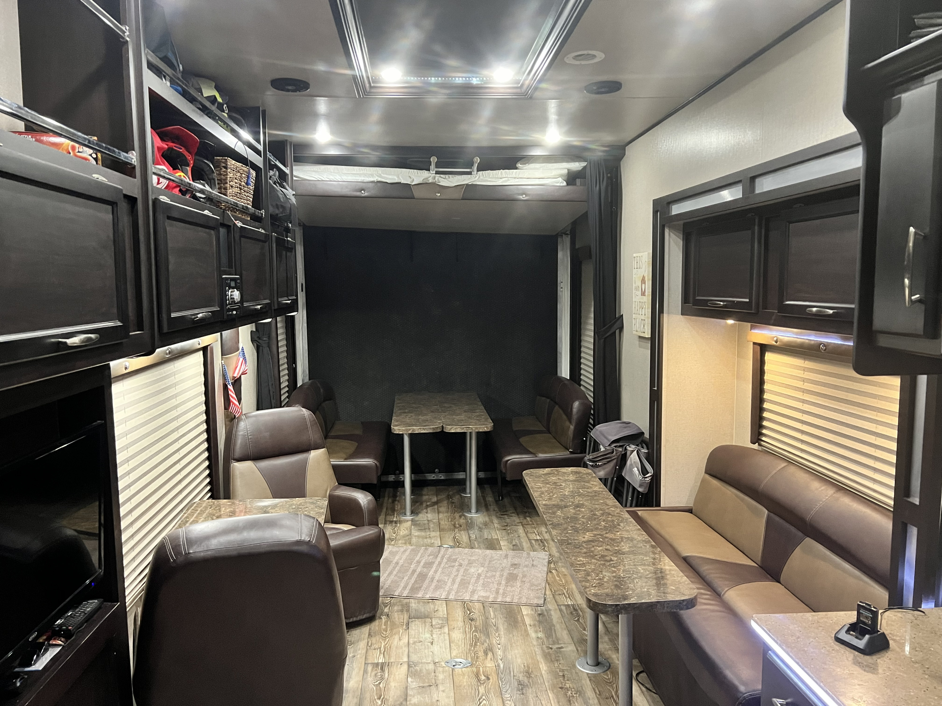 Inside a cozy RV rental: brown leather seating, dining tables, overhead storage, and wood-patterned floors create a homey travel space.. Genesis Supreme Rv Genesis Supreme 2017