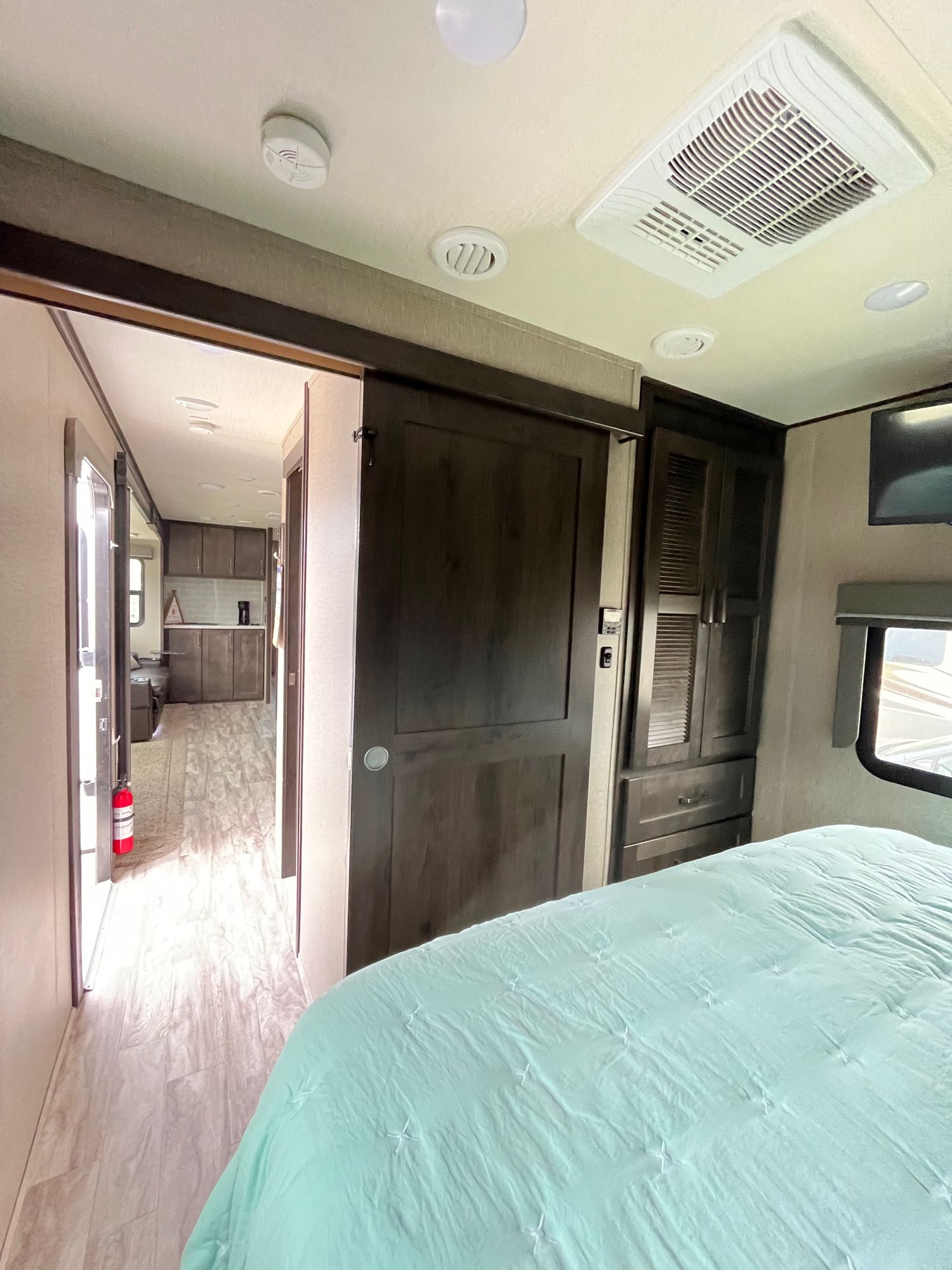 Inside an RV rental bedroom with a blue comforter, showing a sliding door leading to the kitchen and living area.. Grand Design Reflection 2022