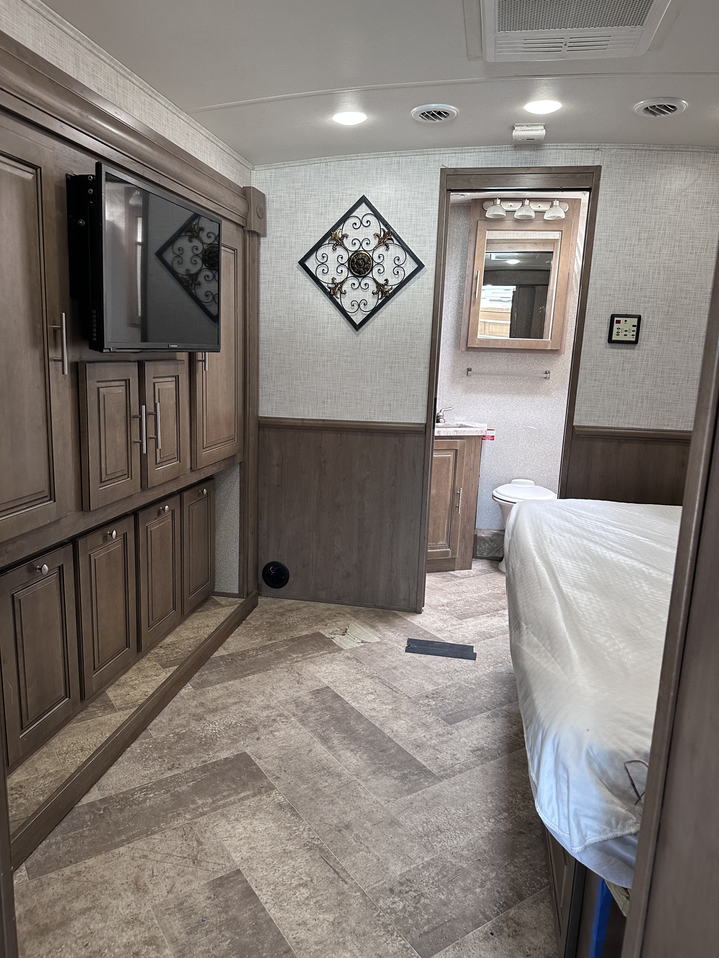 Inside an RV rental: view of a bedroom with a white-sheeted bed, leading to a compact bathroom and built-in entertainment area.. Georgetown GT5 2018