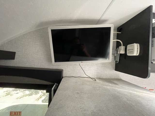 RV rental interior features a mounted LG TV above a bunk bed. An "EXIT" sign visible in the window hints at mobile lodging.. Braxton Creek BUSHWHACKER PLUS 17FD 2022