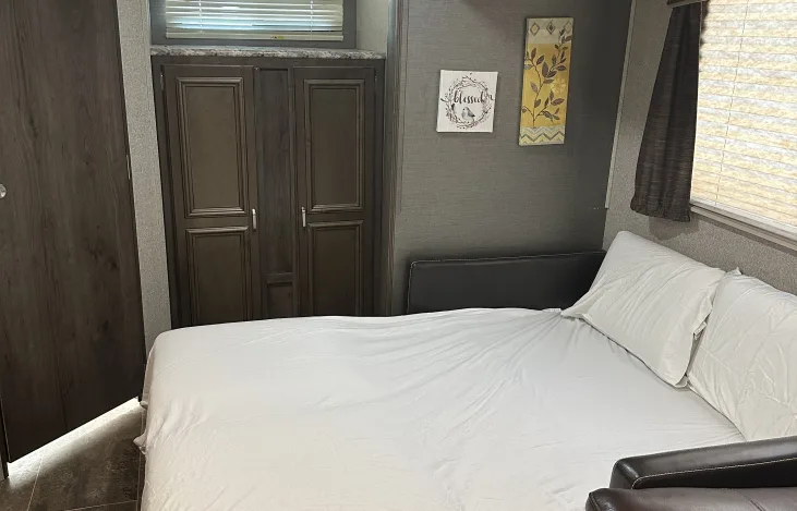 RV rental bedroom: white bed, dark storage cabinets, and wall decor. Cozy and compact RV interior.. Keystone RV Passport Grand Touring 2019