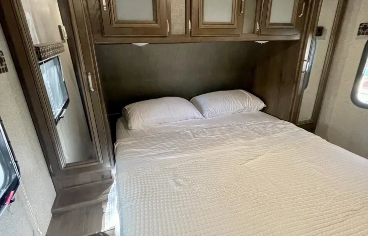 RV rental bedroom: a neatly made bed with white linens, overhead cabinets, and side storage.. Keystone RV Passport Grand Touring 2019
