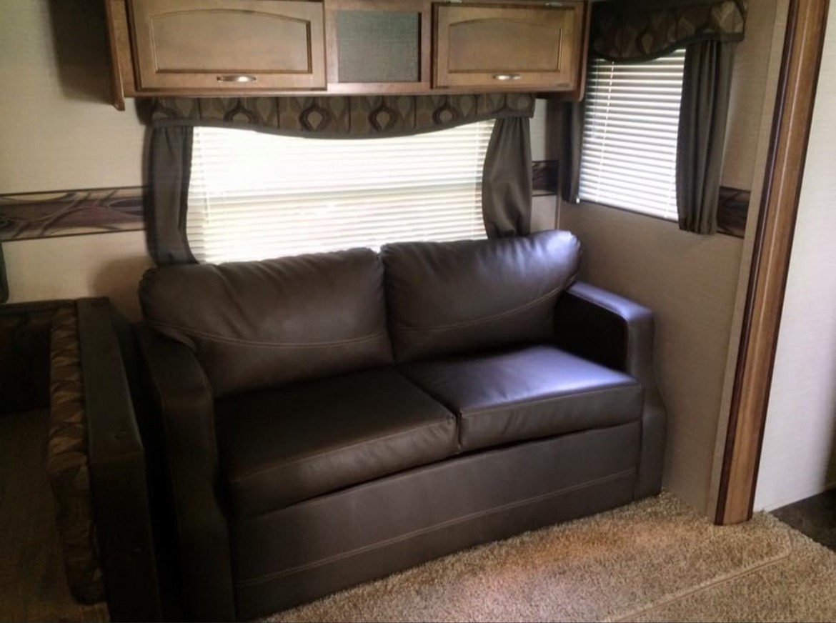 This rv rental offers a comfy brown sofa, overhead storage, and window blinds, perfect for relaxing after a day of travel.. Keystone RV Springdale 2015