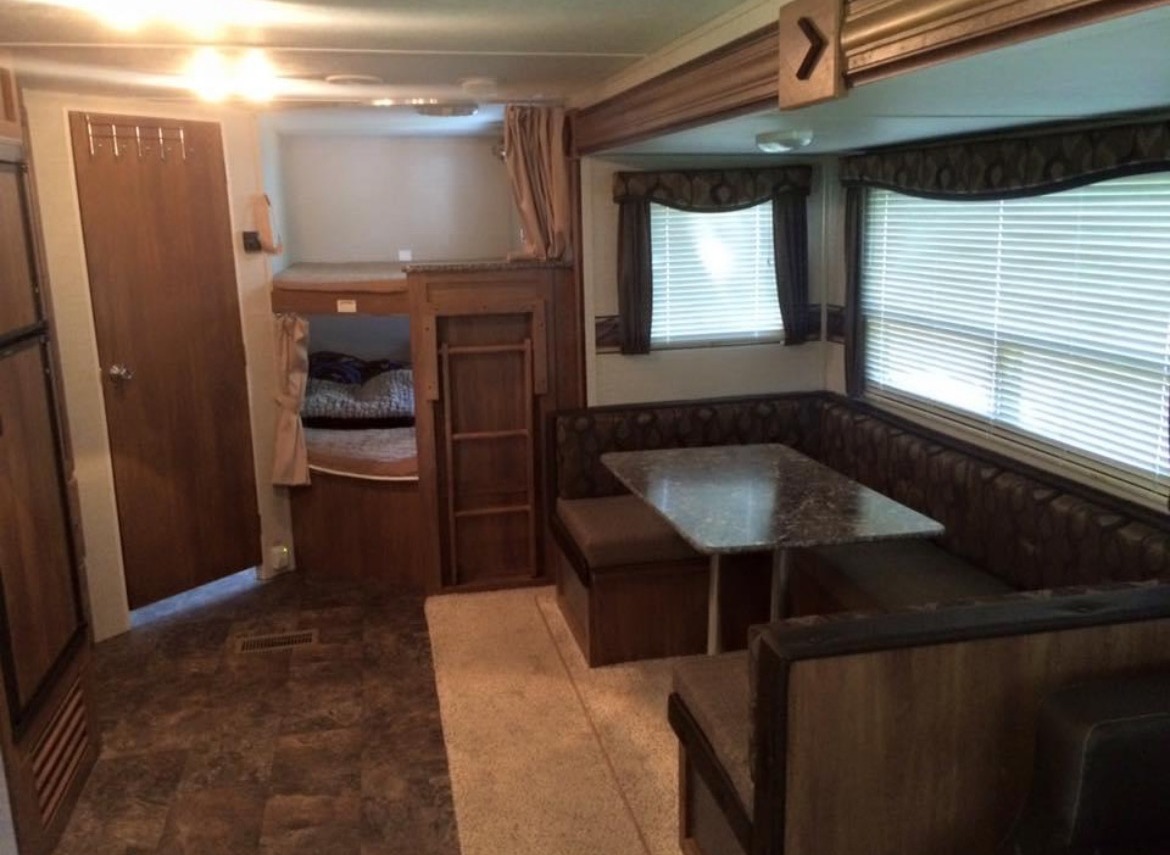 This RV rental interior features a U-shaped dinette, a small table, and built-in bunk beds, ideal for family travel.. Keystone RV Springdale 2015