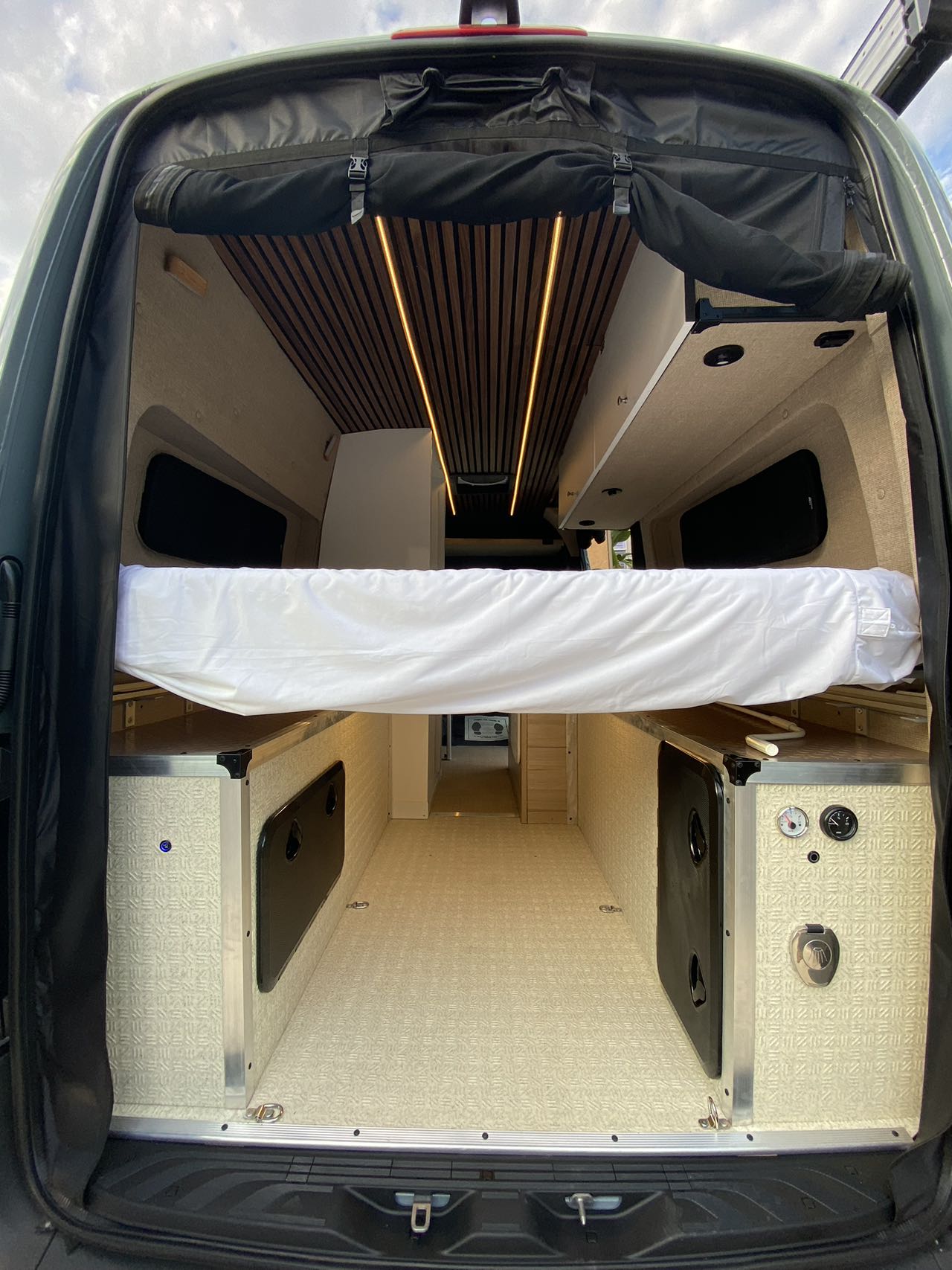 Spacious RV rental interior: custom camper van with raised bed, wood-slat ceiling lights, and smart storage for travel.. Mercedes Benz Sprinter 2500 2022