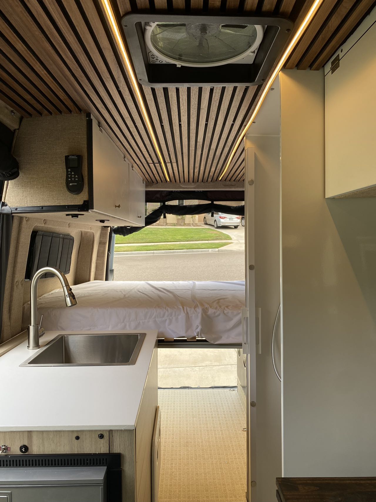 RV rental interior featuring a stylish kitchenette, cozy bed, and custom wood-slatted ceiling with accent lights.. Mercedes Benz Sprinter 2500 2022