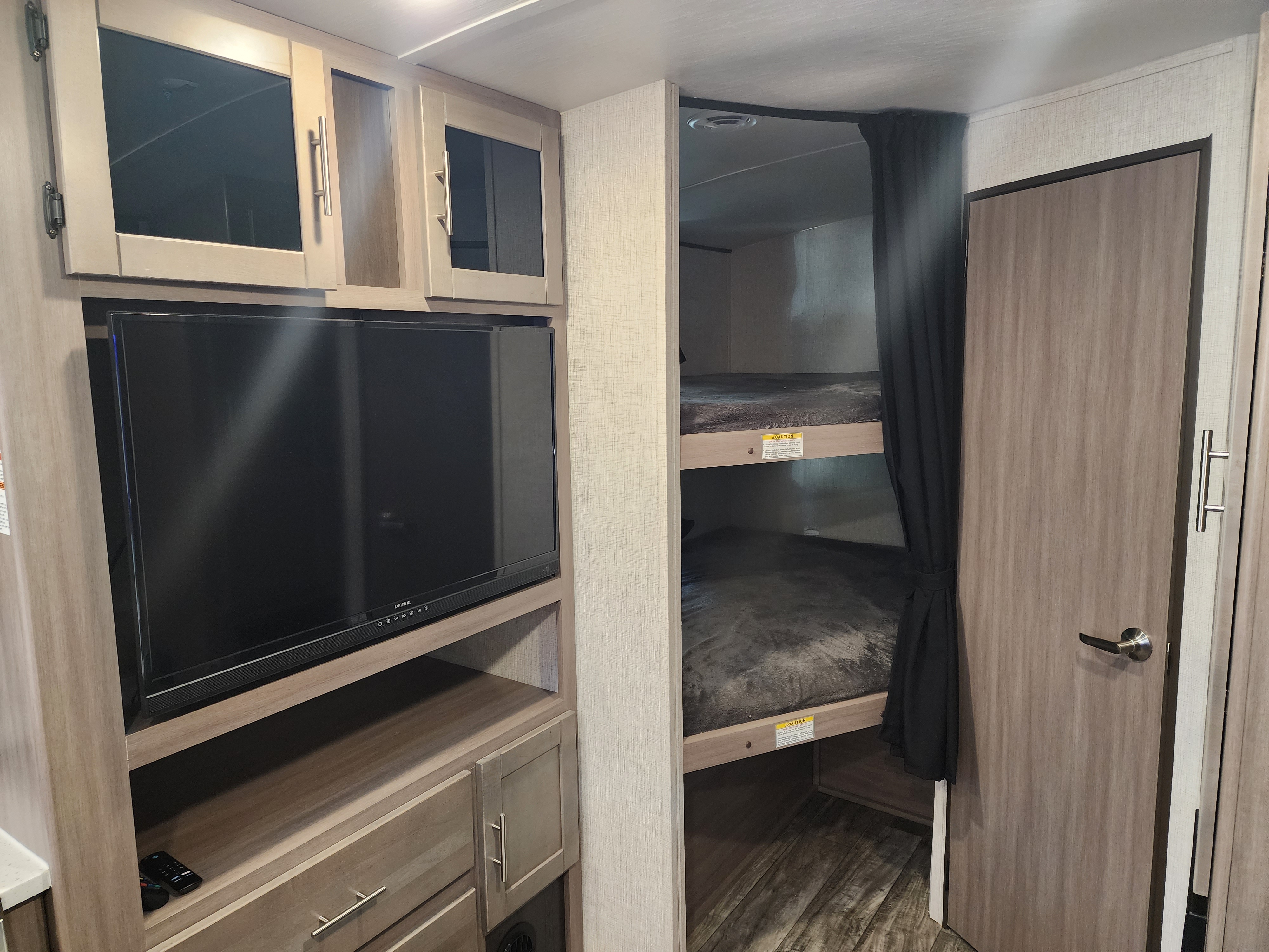 RV rental interior featuring a TV and cabinetry on the left, with cozy bunk beds and privacy curtains on the right.. Crossroads RV Sunset Trail Super Lite 2022