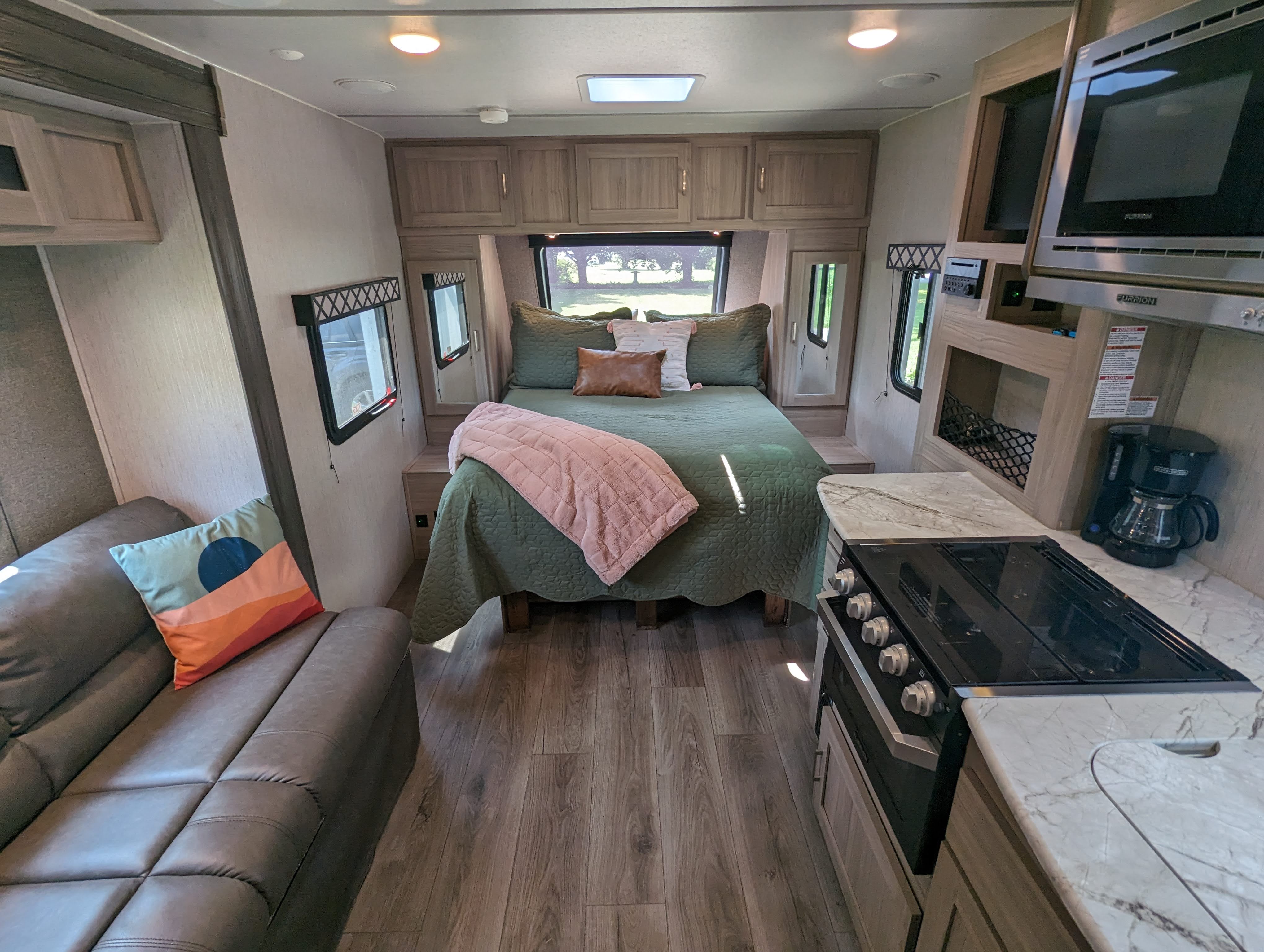 RV rental interior: comfy bedroom with green bedding, full kitchen, and sofa. Wood-look flooring throughout.. Forest River Coachmen Freedom Express Ultra Lite 2020
