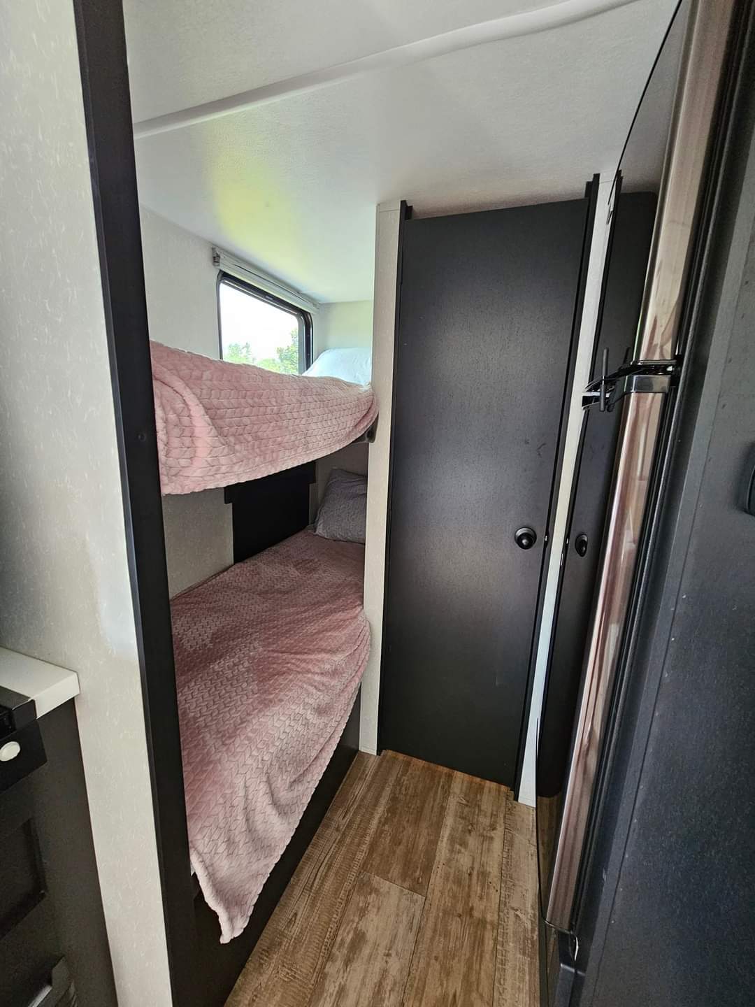An RV rental's interior features cozy bunk beds with pink blankets, a dark door, and wood-look flooring.. Forest River Cherokee Wolf Pup Black Label 2021