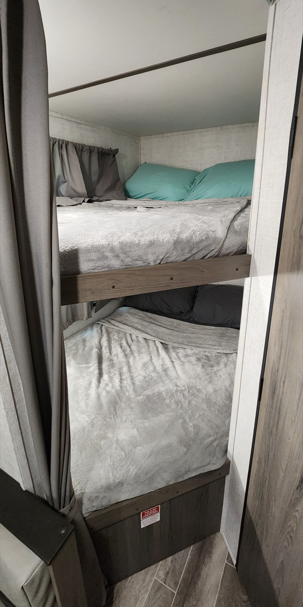 RV rental bunk beds: two cozy sleeping berths with grey blankets and pillows in a modern camper interior.. Gulf Stream Conquest Super Lite 2021