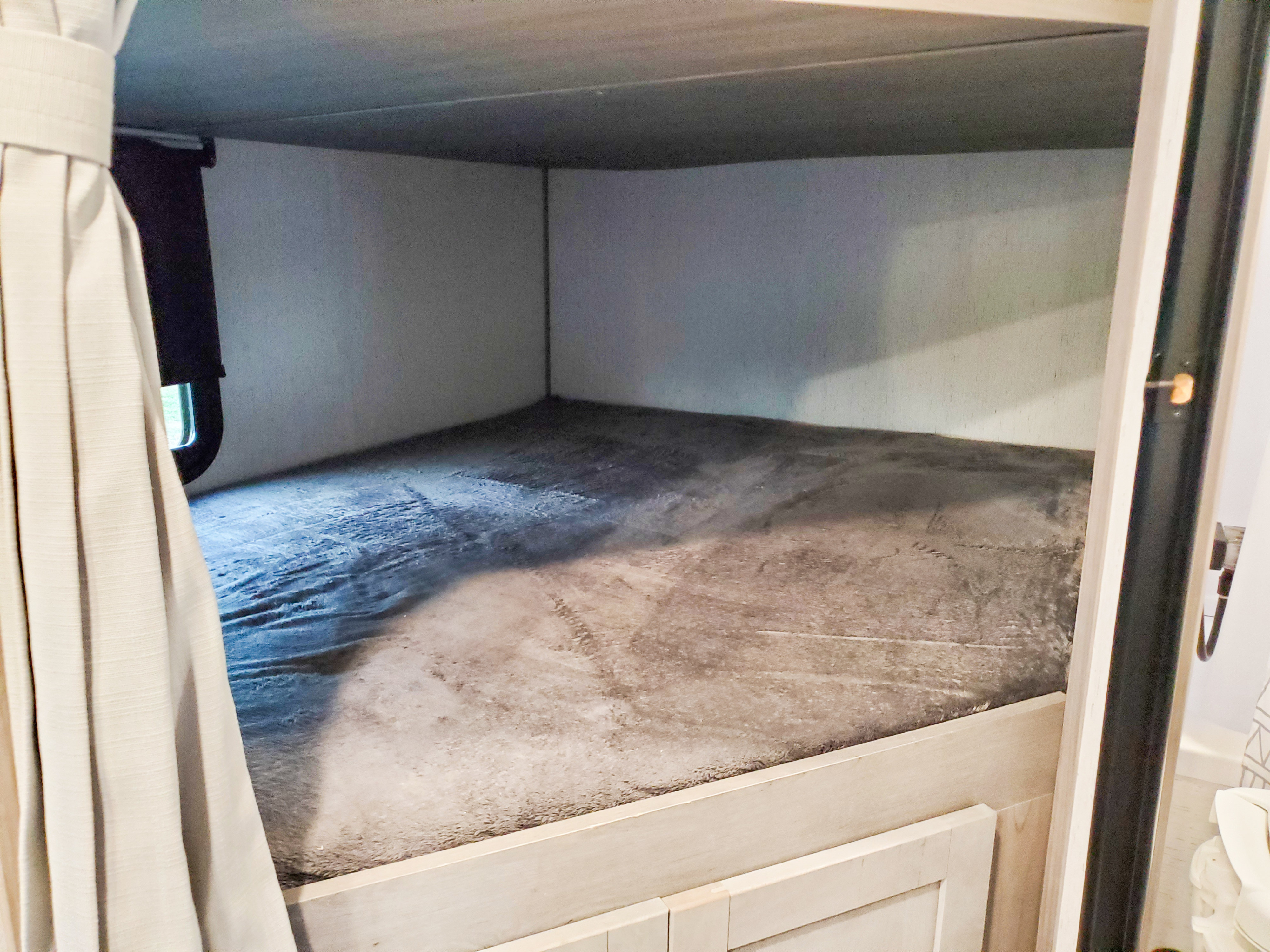 Inside an RV rental: a compact bunk bed with a grey mattress, curtained window, and light wood trim.. Dutchmen Kodiak Ultra Lite 2022