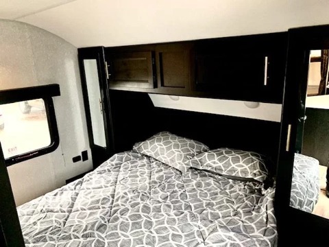 Cozy and functional bedroom inside an RV, ideal for your next rv rental. Features a bed, overhead storage, and a window.. Forest River Cherokee Grey Wolf 2022