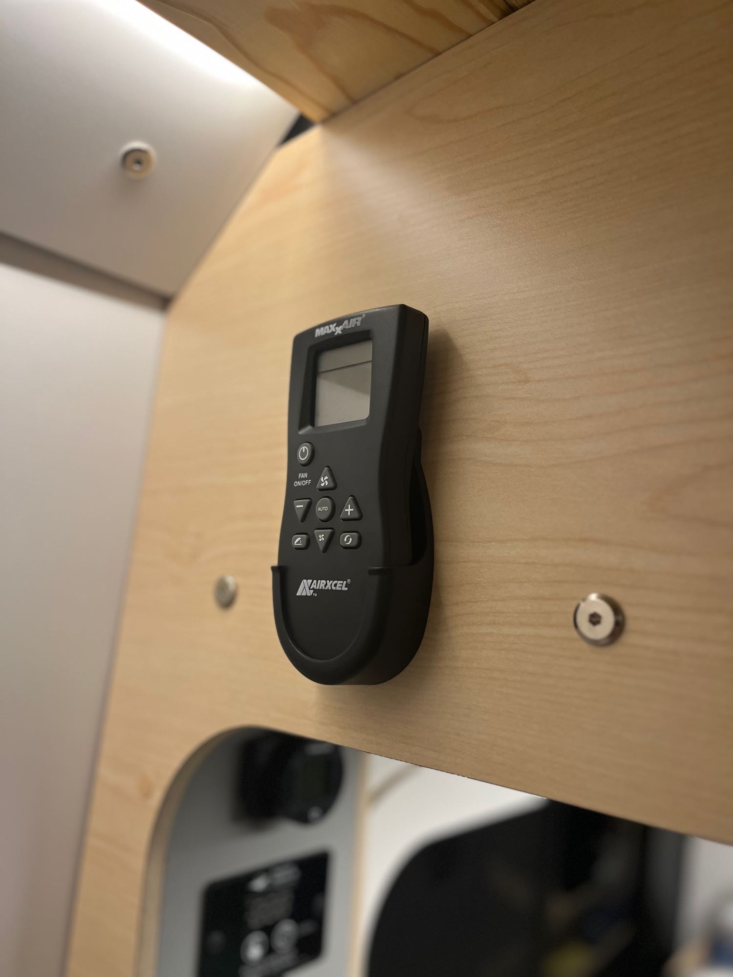 A Maxx-Air fan remote control in its holder, mounted on a light wood panel, commonly seen in an RV rental for climate control.. DM Vans LV7 2022