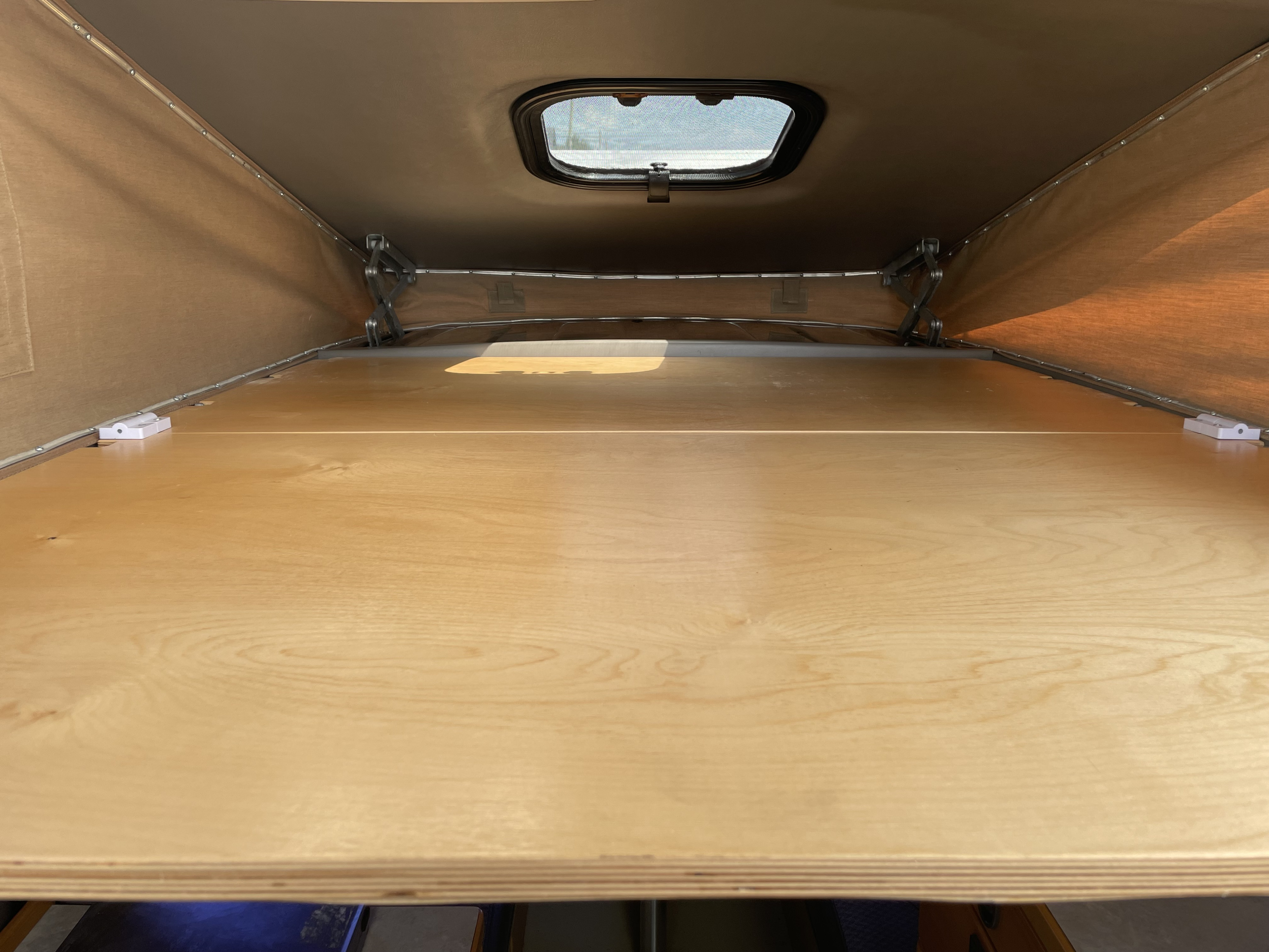 Spacious pop-top sleeping area inside an RV rental. Light wood platform ready for adventure.. Chevrolet New West 2000